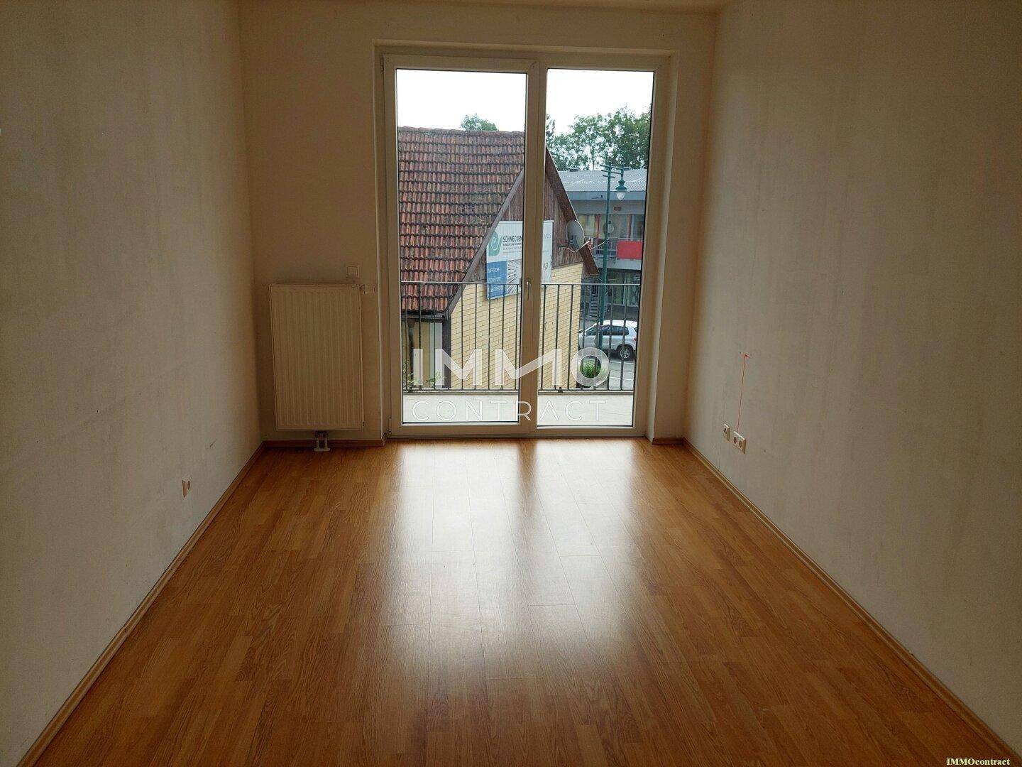 Lichtdurchflutetes Zimmer mit Holzboden und großem Fenster mit Blick nach draußen.