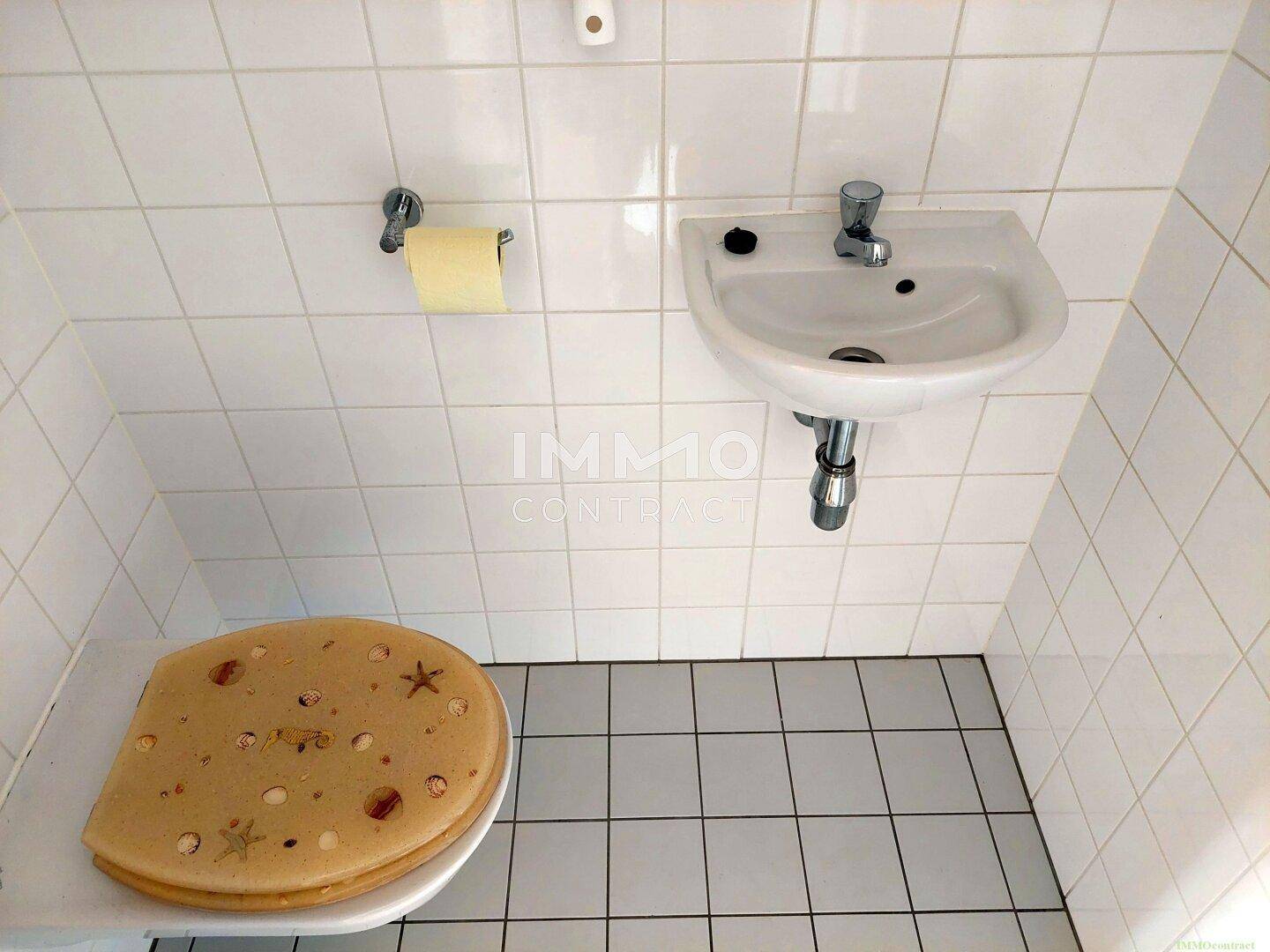 Separate Toilette mit Waschbecken und weißen Wand- und Bodenfliesen.