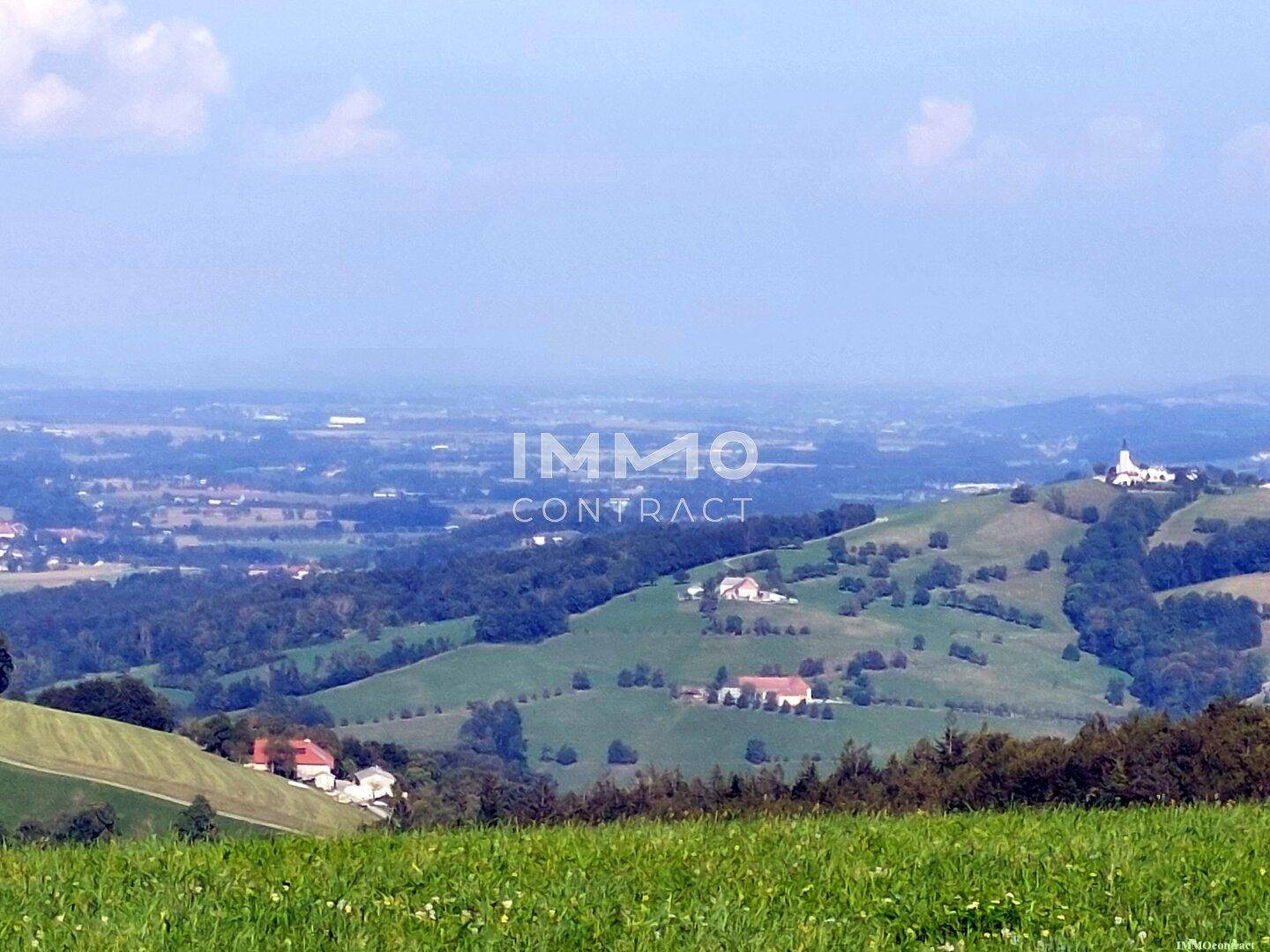 Weitläufiger Panoramablick über die grüne Hügellandschaft mit vereinzelten Häusern.