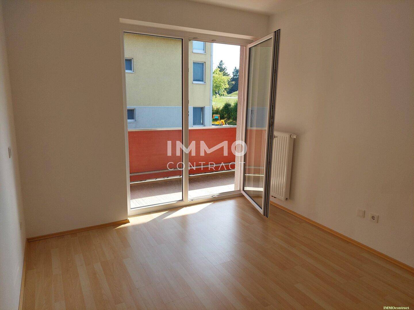 Heller Raum mit Laminatboden und großem Balkonzugang, ideal als Wohn- oder Schlafzimmer.