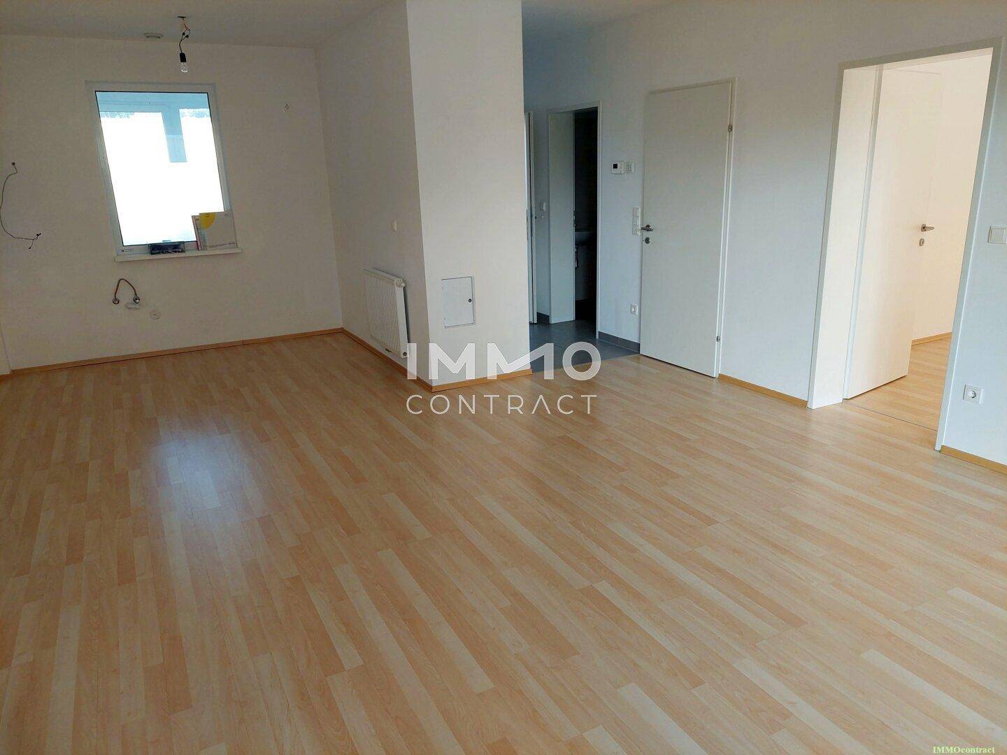 Geräumiger, unmöblierter Wohnbereich mit hellem Laminatboden und großem Fenster.