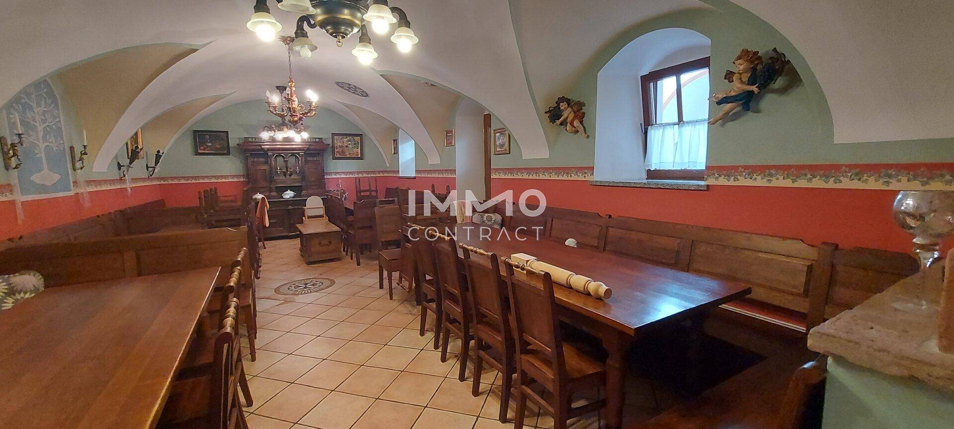 Ein traditioneller Speisesaal mit Gewölbedecken, Holzbänken und Tischen, dekoriert mit klassischen Gemälden.