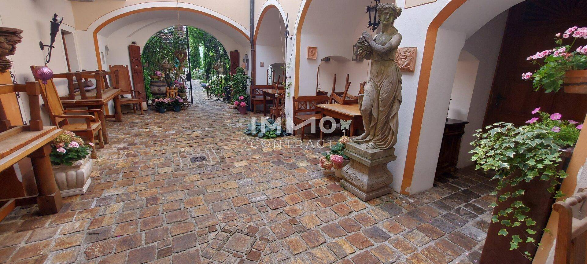 Ein weitläufiger Innenhof mit Kopfsteinpflaster, umgeben von historischen Gebäudeteilen und einer klassischen Statue.