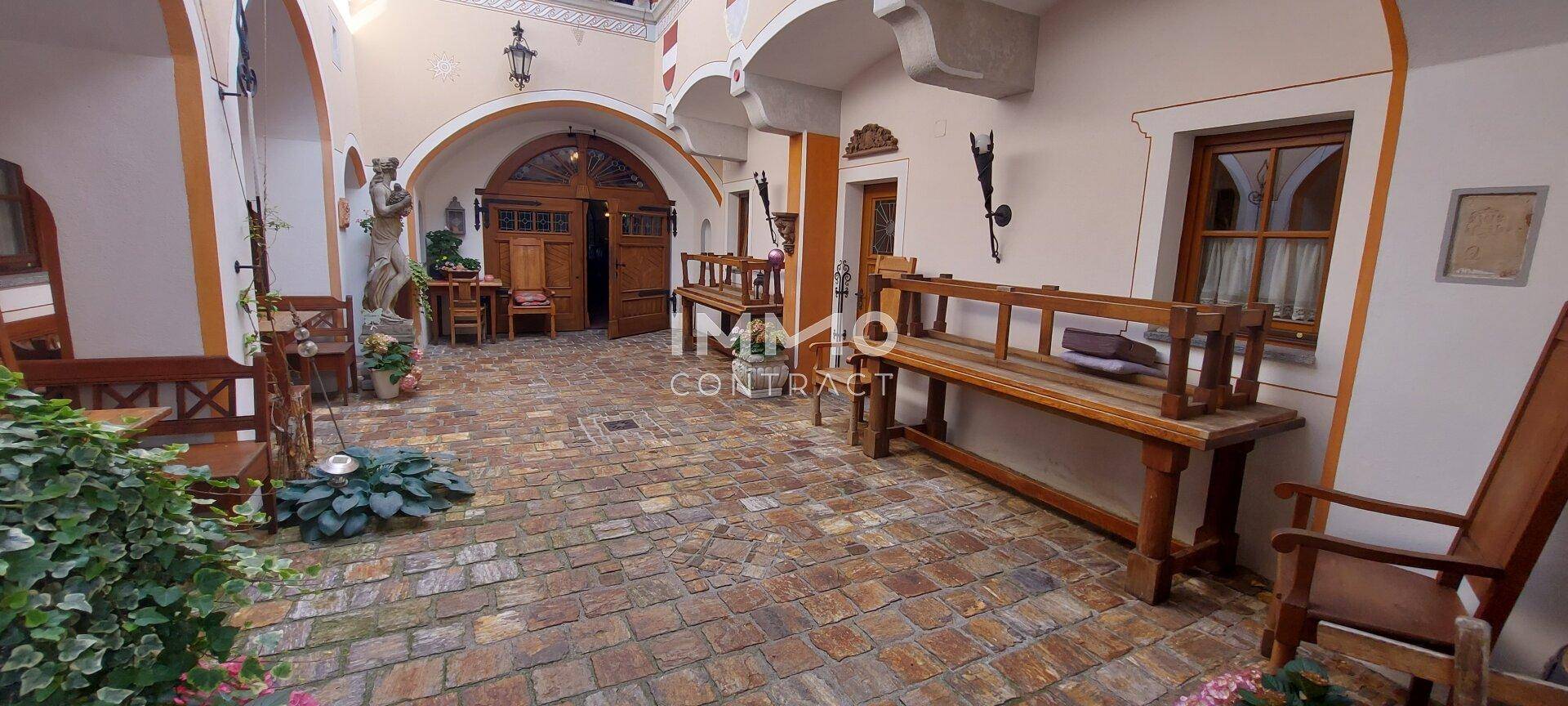 Ein traditioneller Innenhof mit Kopfsteinpflaster, Holzbänken und Arkaden, die das historische Ambiente unterstreichen.