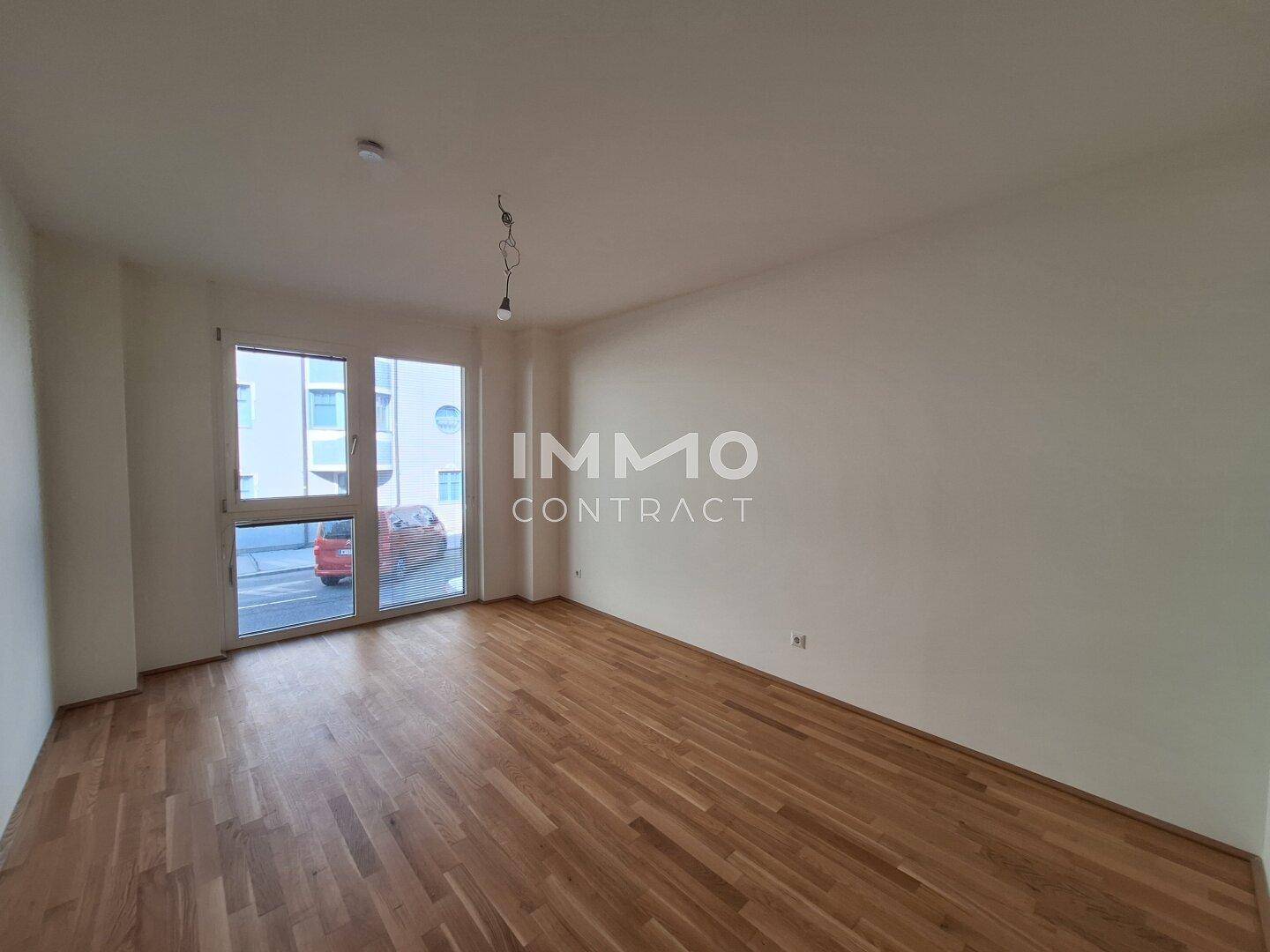 Helles Zimmer mit Parkettboden und großem Fenster, das viel Tageslicht hereinlässt.