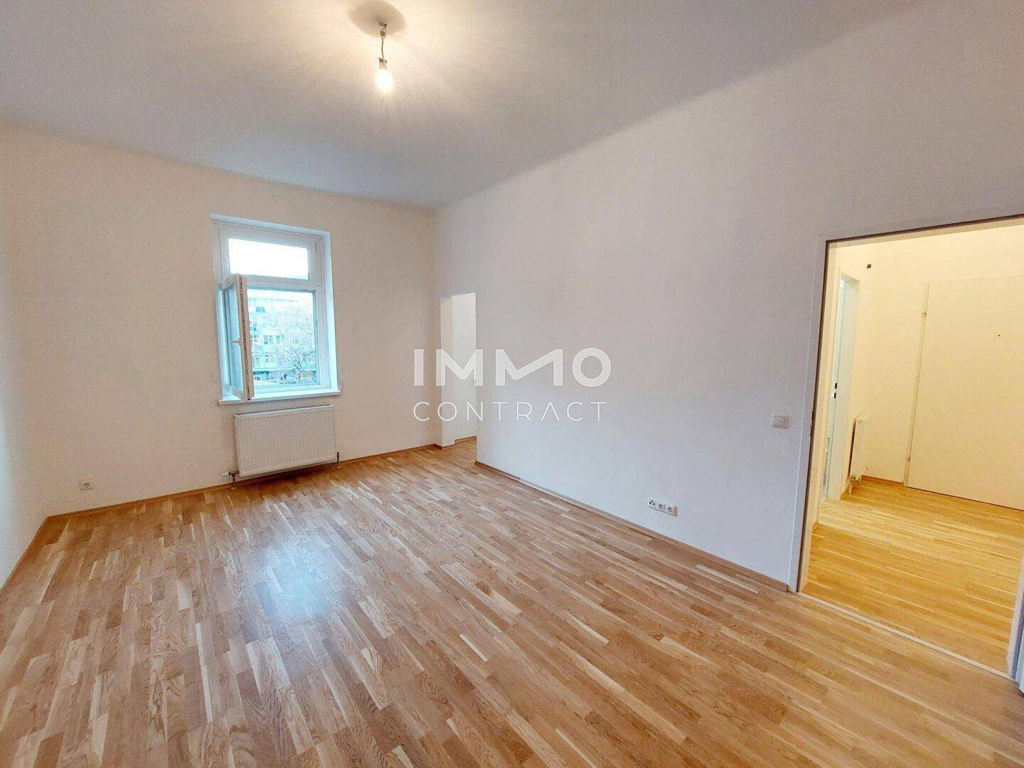 Geräumiges, leeres Zimmer mit hellem Parkettboden und einem großen Fenster, bereit zur Einrichtung.
