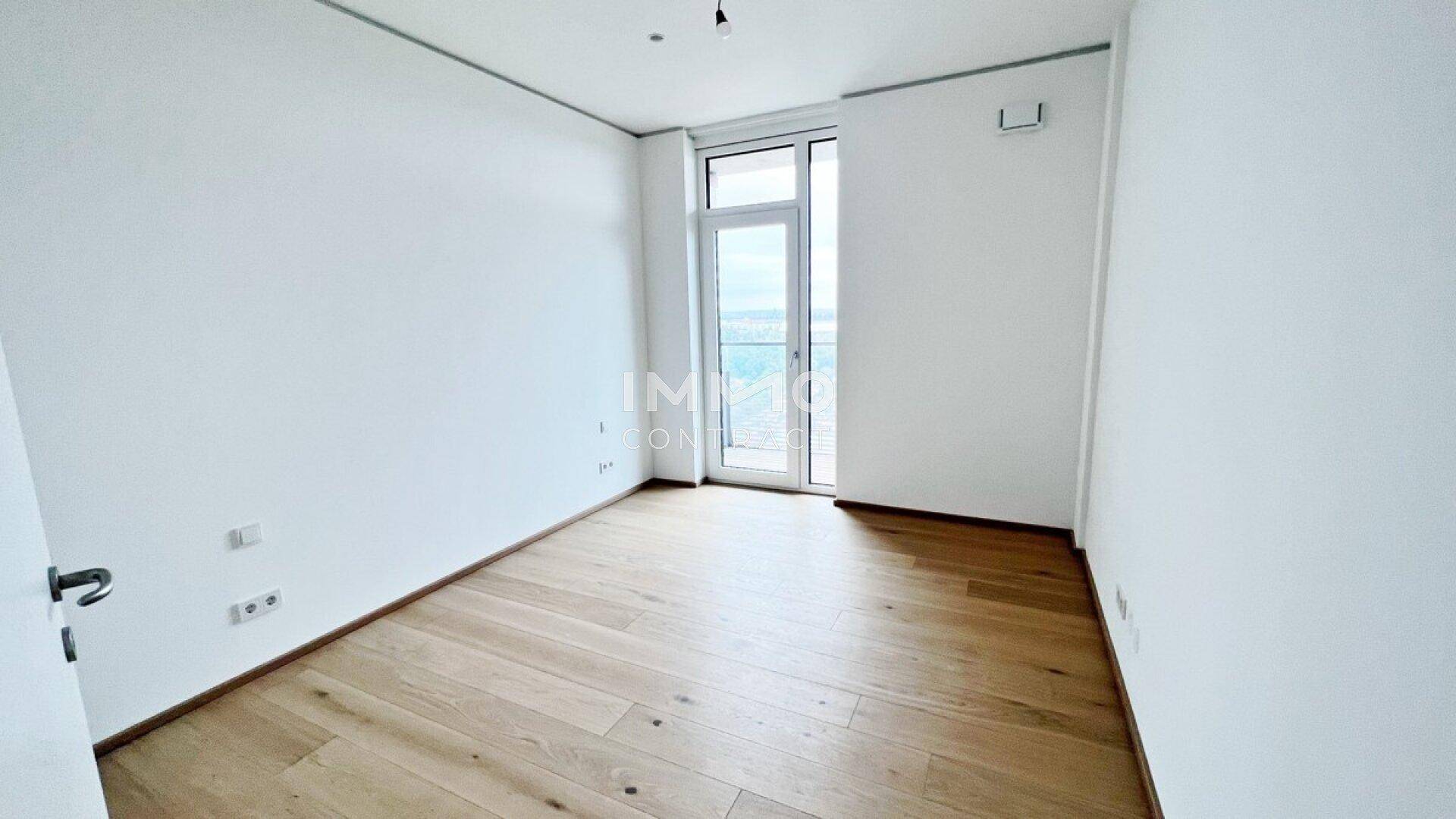 Helles Zimmer mit Holzboden und Zugang zu einem Balkon, ideal als Schlafzimmer oder Büro.