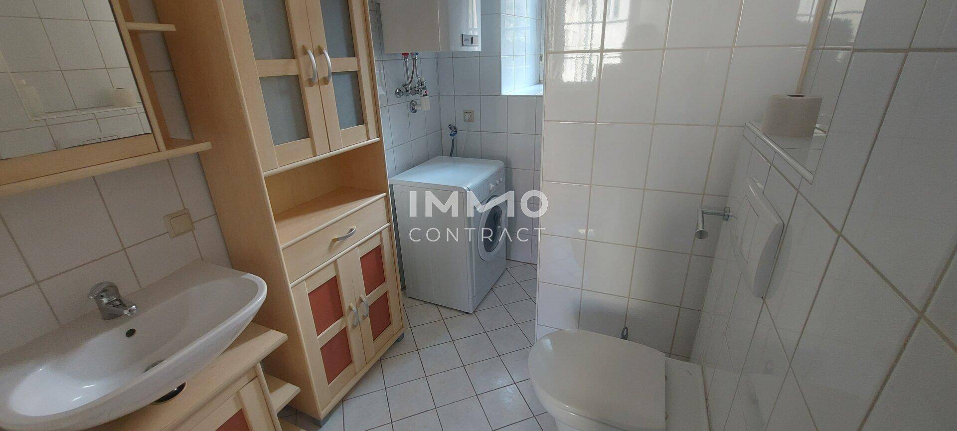 Badezimmer mit WC, Waschbecken, Spiegelschrank und Waschmaschine, komplett gefliest.