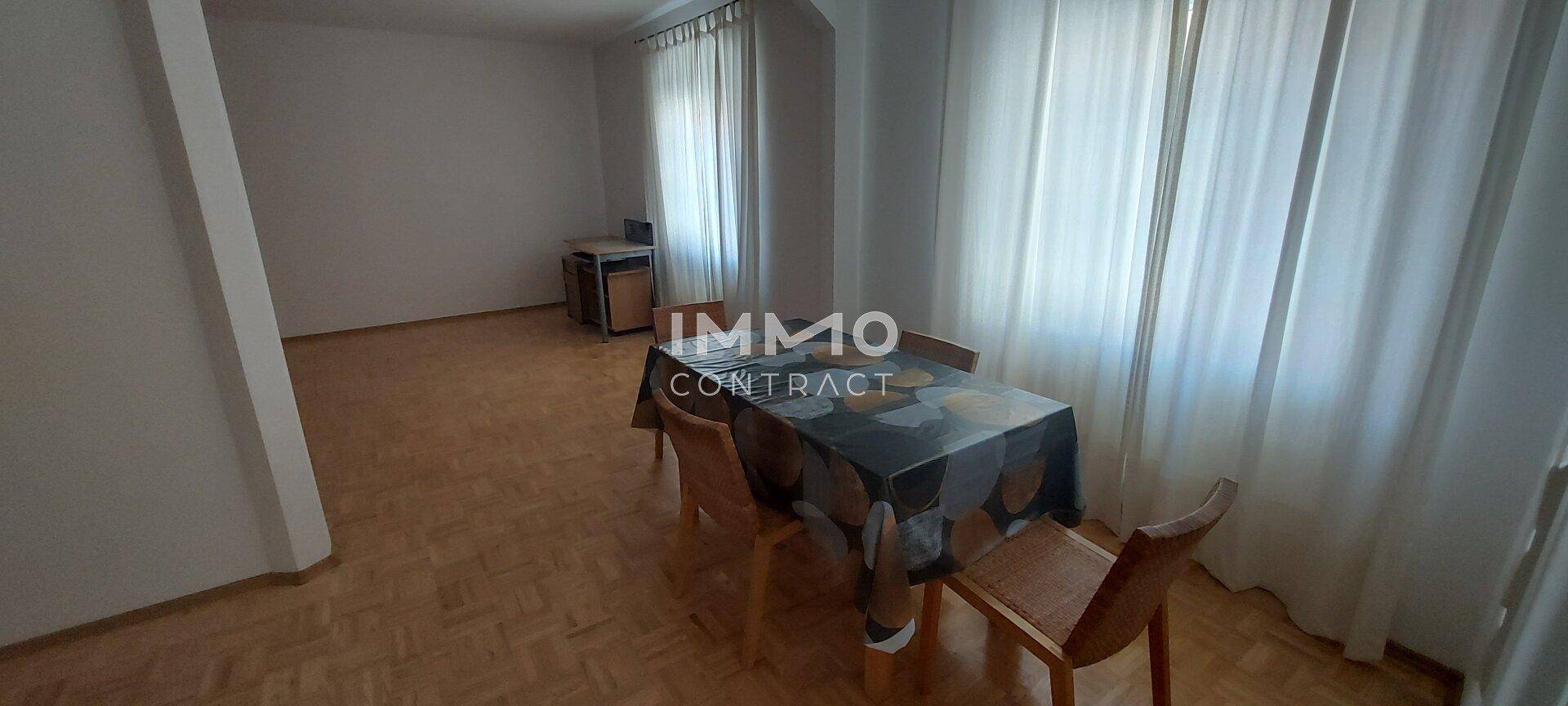 Essbereich mit Holztisch und Stühlen, umgeben von hellen Vorhängen und Parkettboden.