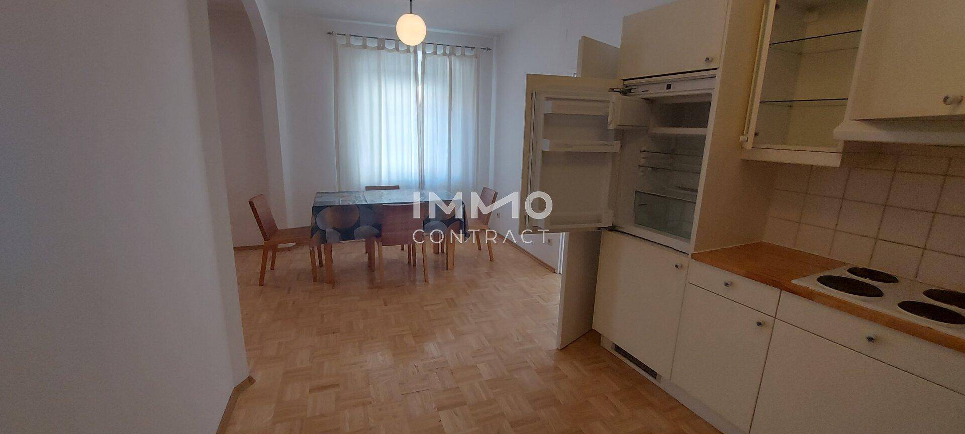 Kombinierter Küchen- und Essbereich mit Einbauküche, Kühlschrank und Esstisch auf Parkettboden.