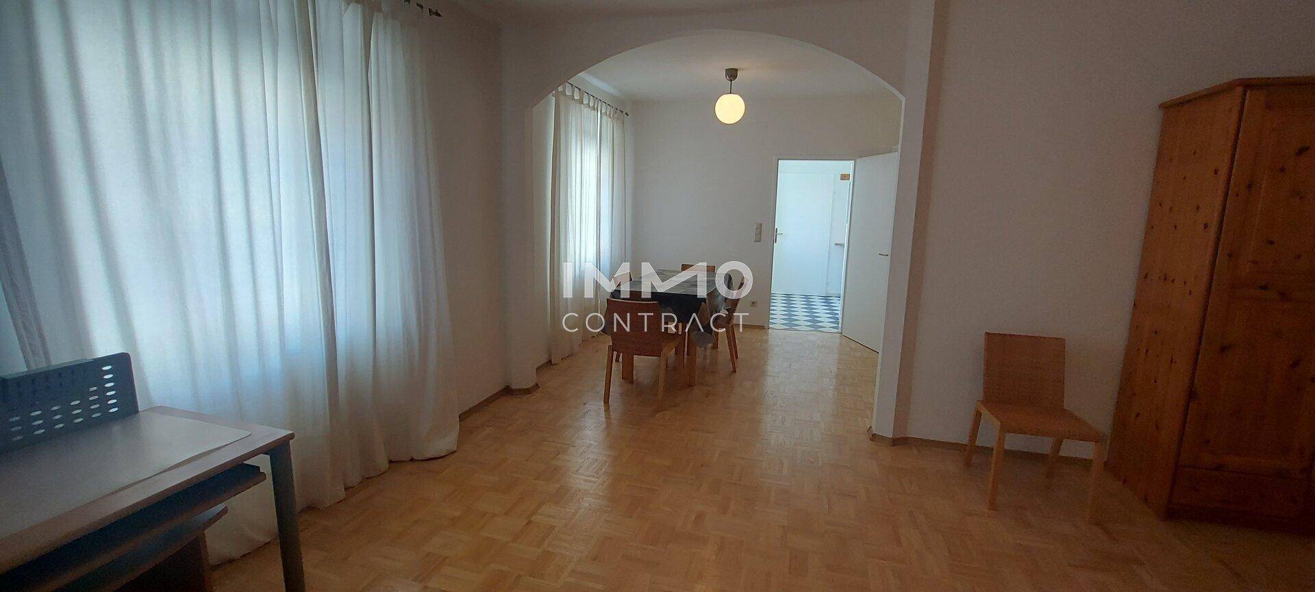 Heller Wohn- und Essbereich mit Parkettboden, einem Bogen und Blick in einen gefliesten Raum.