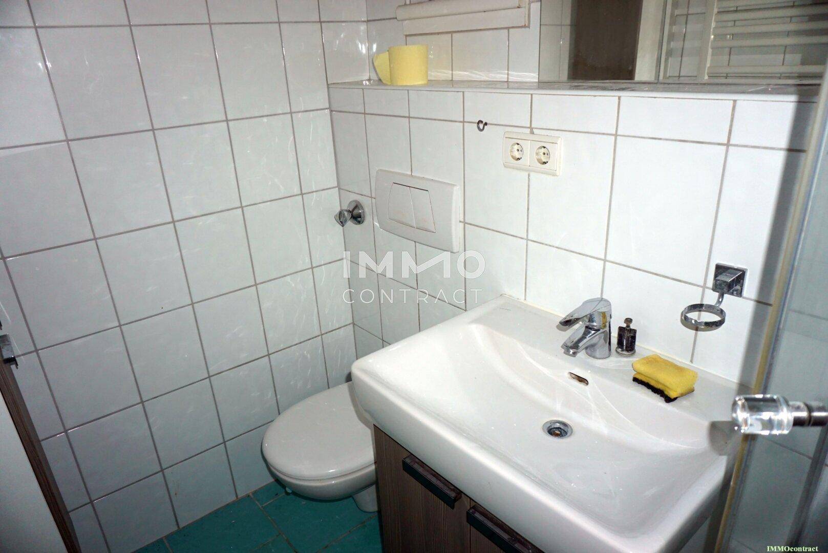 Kleines Badezimmer mit WC, Waschbecken und weißen Wandfliesen in einfacher Ausführung.