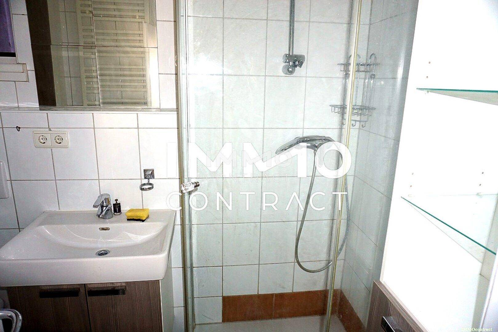 Badezimmer mit Duschkabine, Waschbecken und weißen Fliesen an den Wänden in Standardausführung.