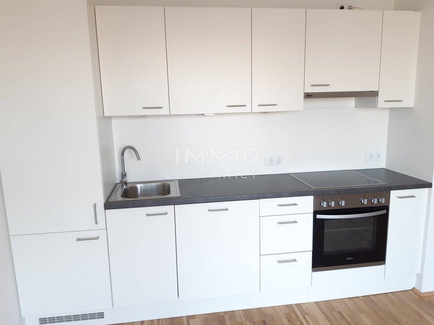 Moderne Einbauküche mit weißen Schränken, dunkler Arbeitsplatte und Kochfeld.