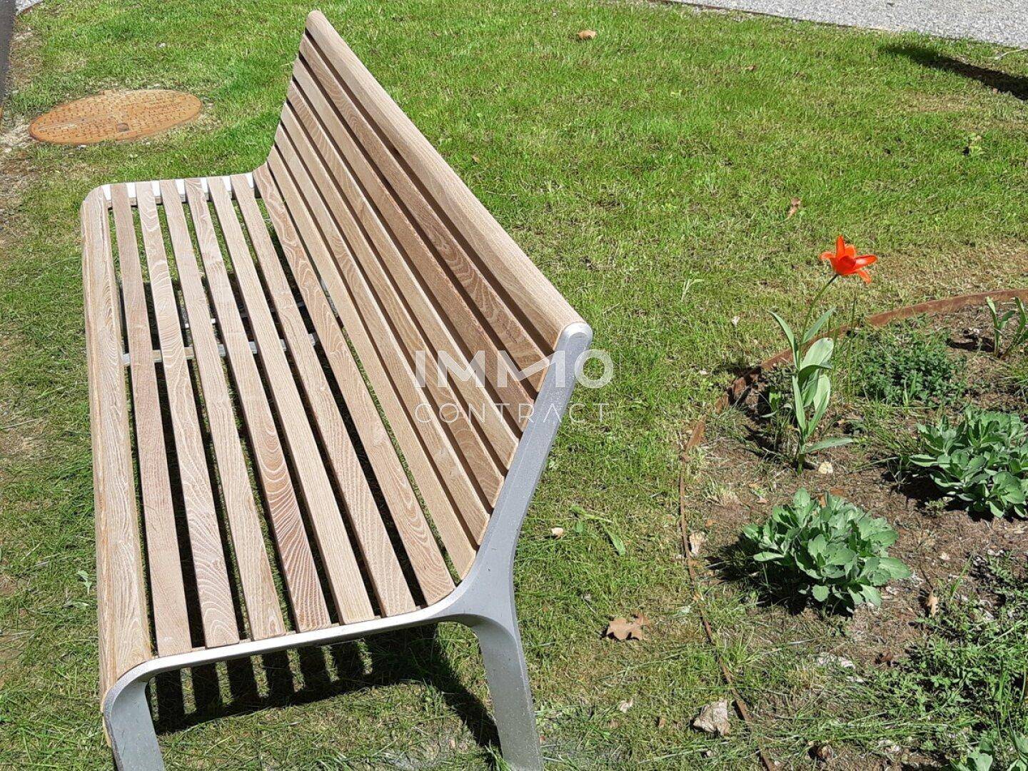 Moderne Holzbank im Gartenbereich neben einer kleinen Pflanze.