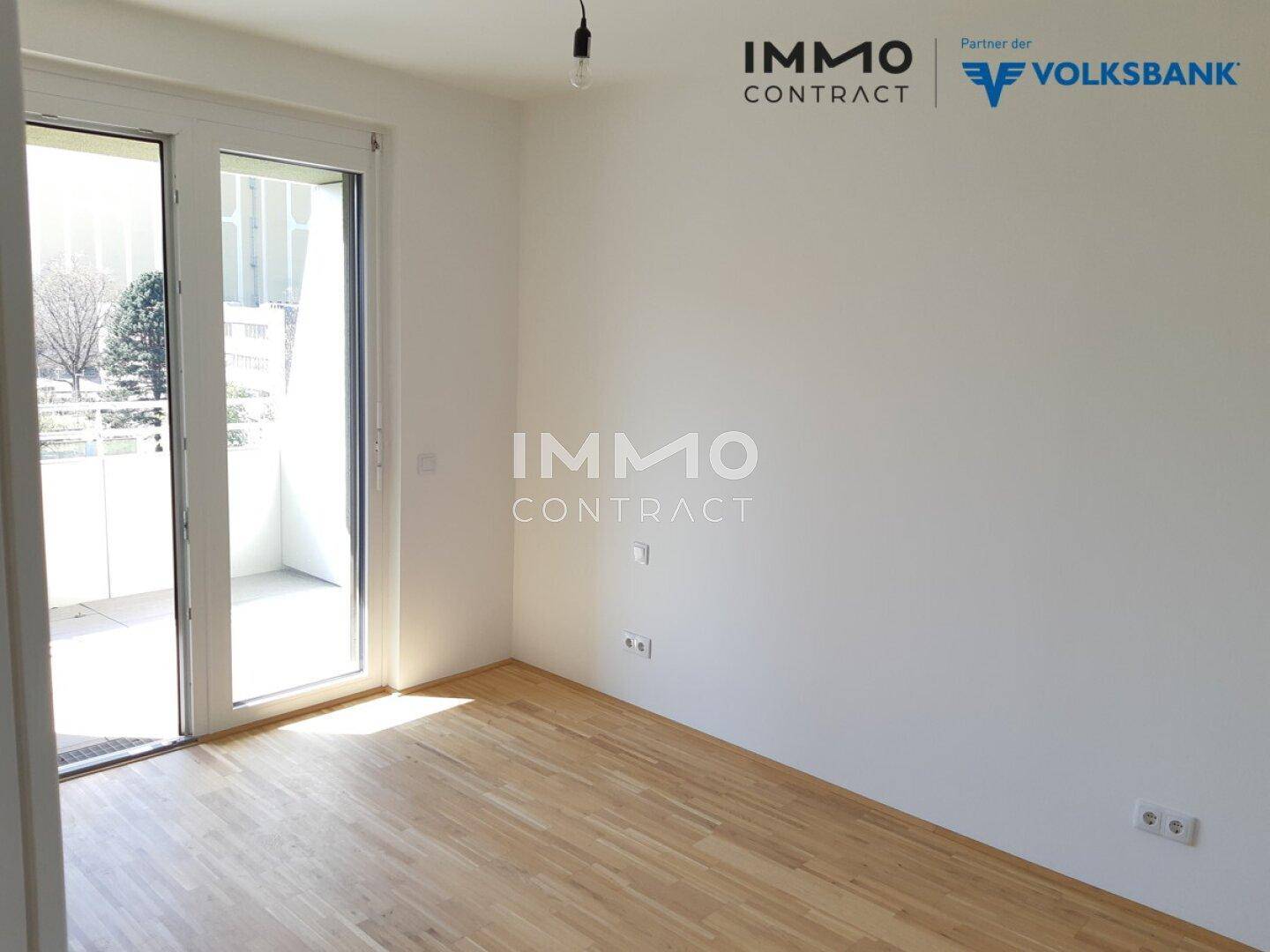 Helles Zimmer mit Holzboden und Zugang zu einem Balkon oder einer Terrasse.