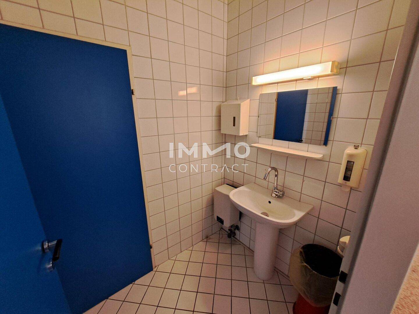 Einfache Toilette mit weiß gefliesten Wänden, Waschbecken und blau gestrichener Tür.