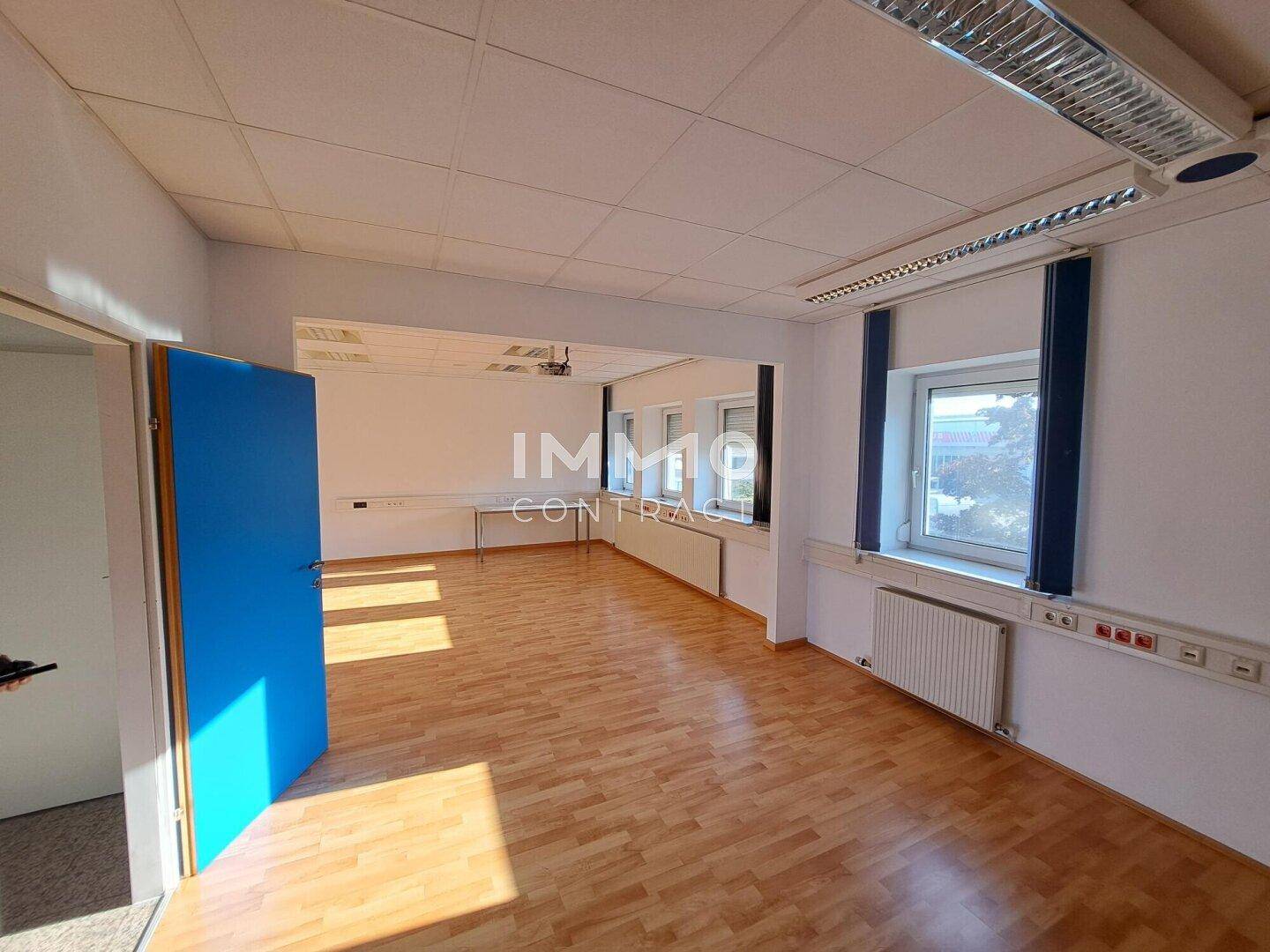 Geräumiges Büro mit Holzboden, weißen Wänden und mehreren Fenstern für viel Tageslicht.