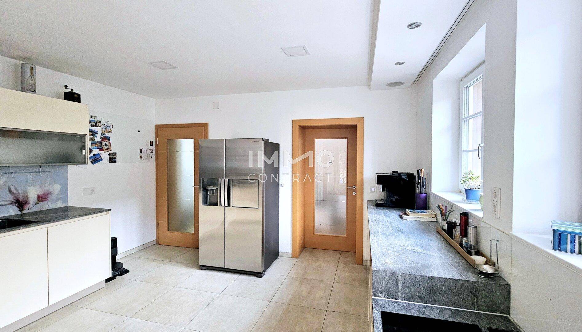 Funktionale Küche mit großem Kühlschrank, hellen Schränken und dunklen Arbeitsplatten.