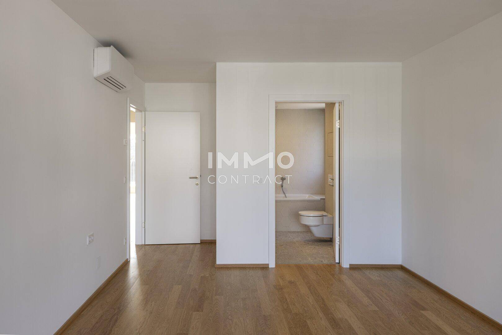 Schlafzimmer mit Holzboden und direktem Zugang zu einem modernen Badezimmer.