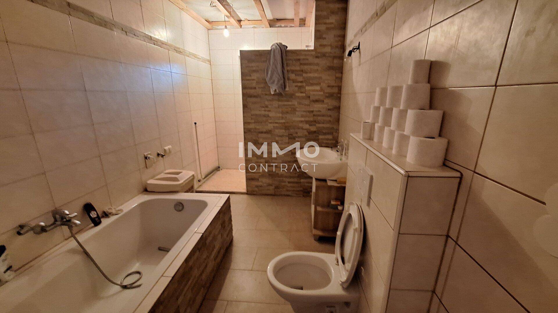 Badezimmer mit Badewanne, Toilette und Fliesen an Wänden und Boden in hellem Farbton.