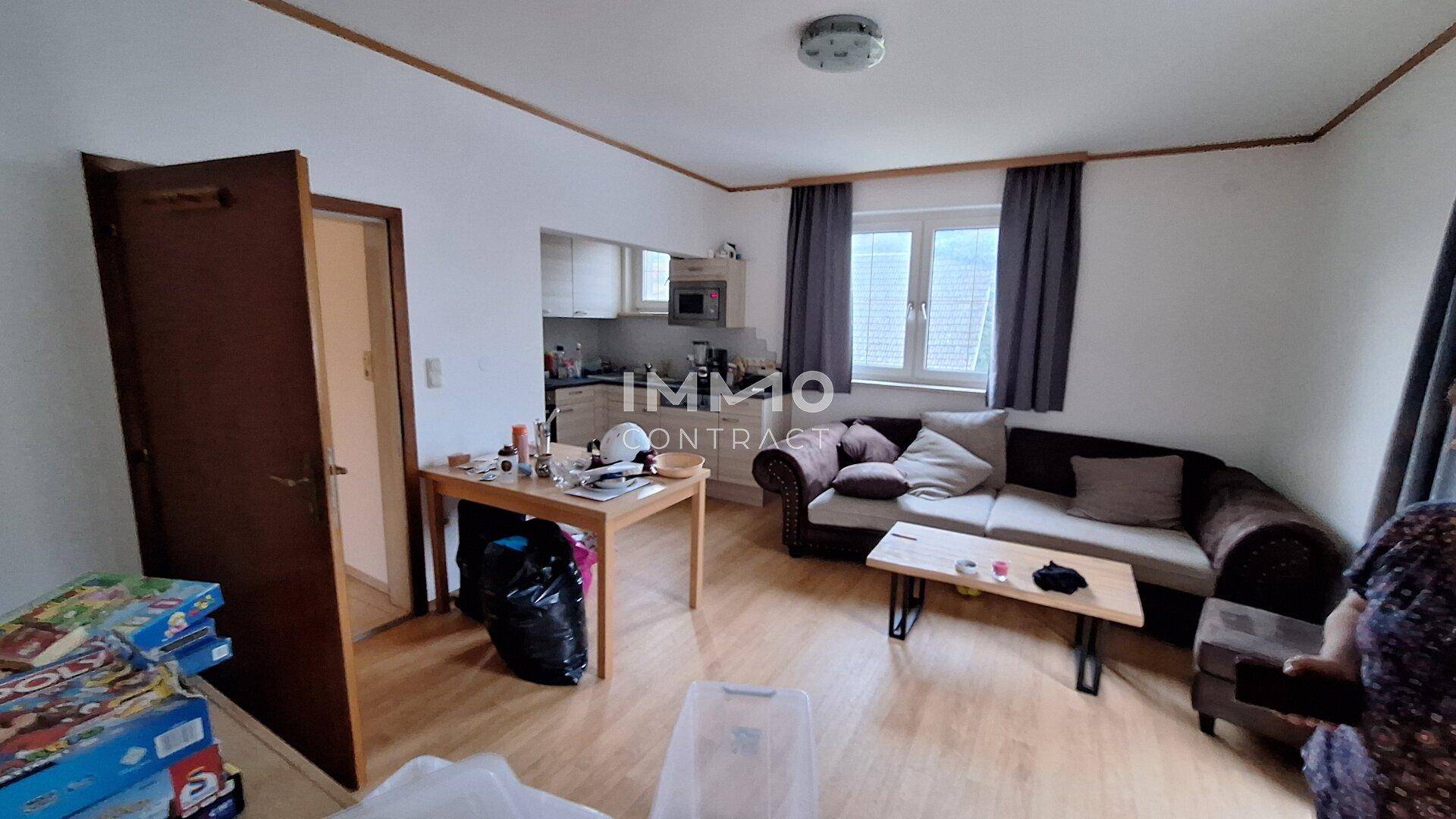 Heller Wohnbereich mit Laminatboden, Sofa und offener Verbindung zur Küche im Hintergrund.