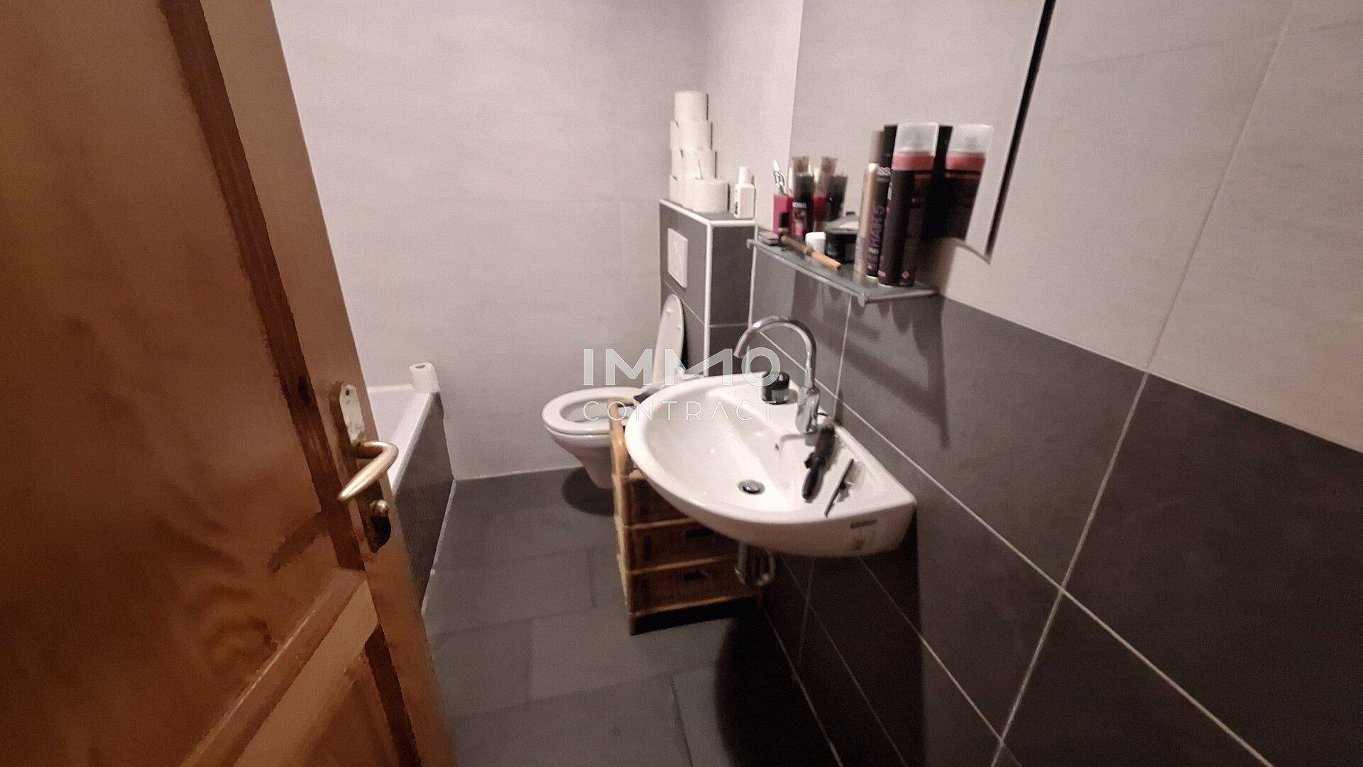 Modernes Badezimmer mit grauen Fliesen, Badewanne, wandhängendem WC und Eckwaschbecken.