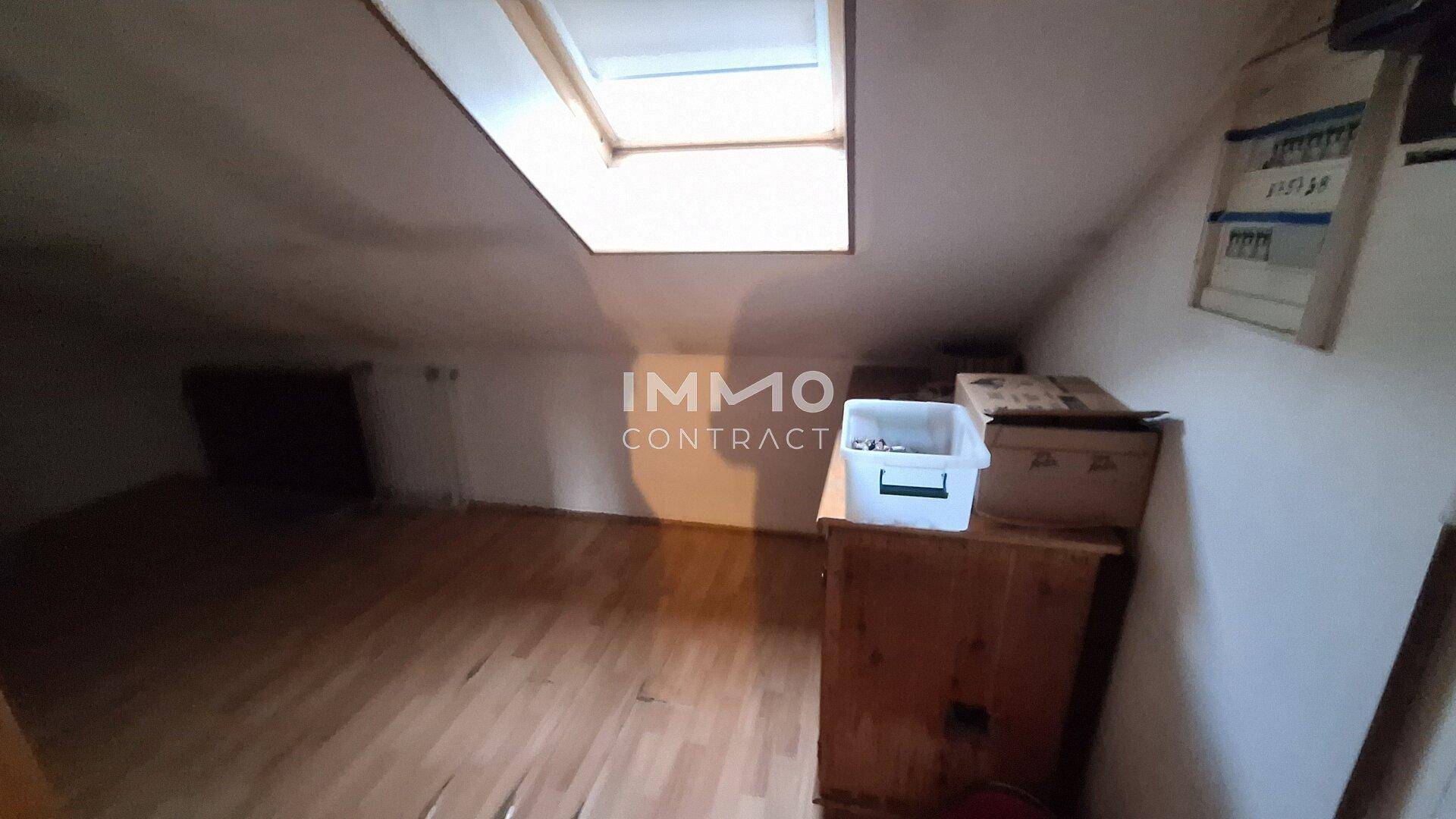 Dachbodenraum mit schrägen Wänden, Holzboden und einem Dachfenster, das für Helligkeit sorgt.