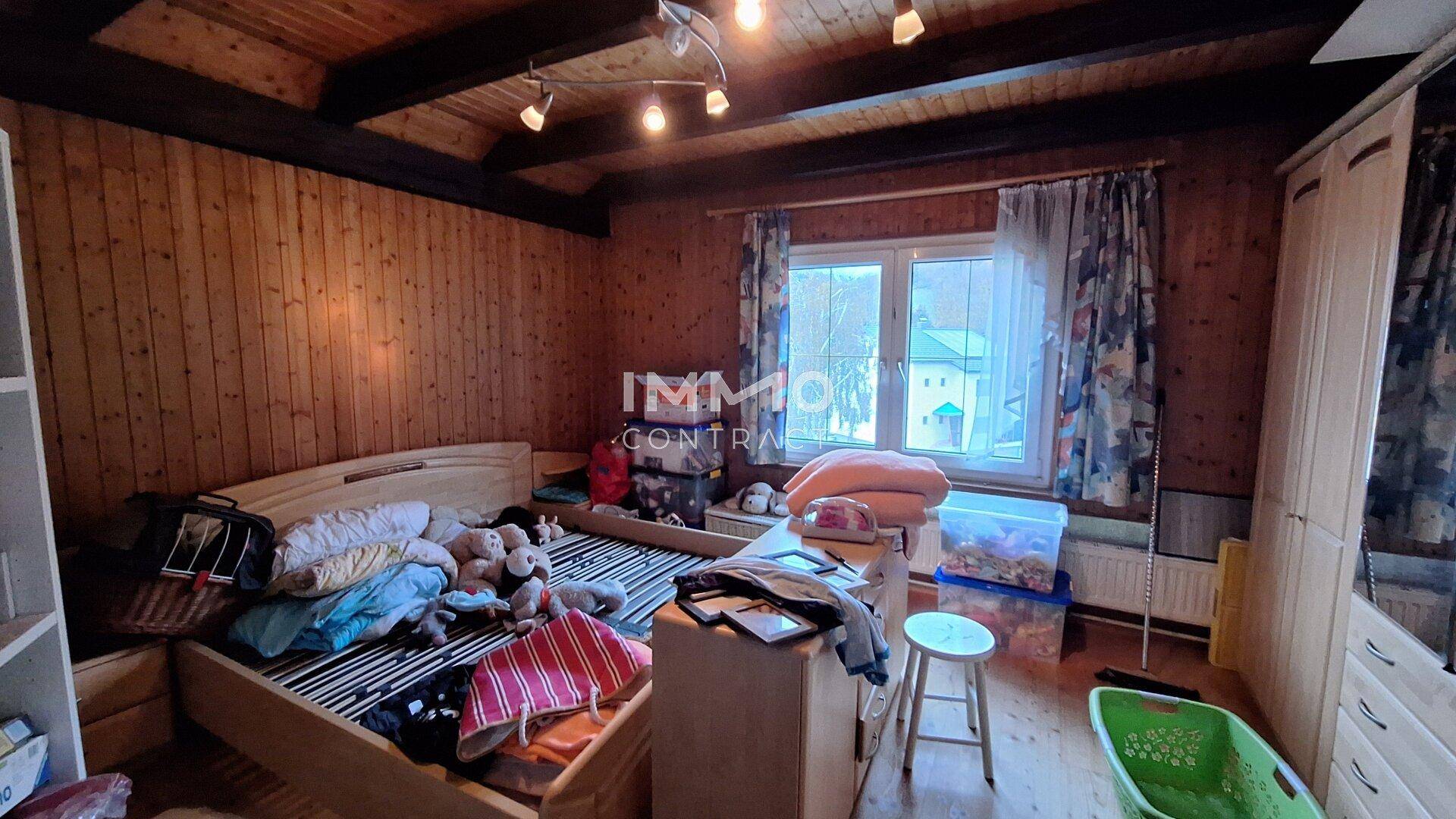 Rustikales Schlafzimmer mit viel Holzverkleidung an Wänden und Decke, sowie einem Fenster.