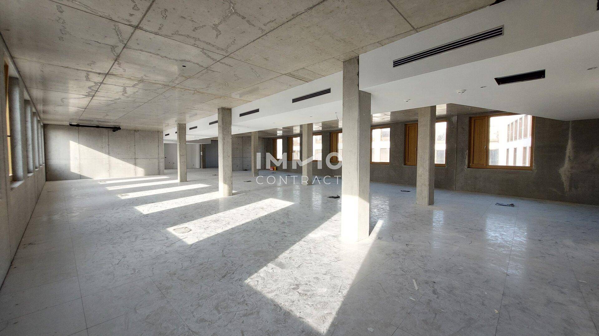 Weitläufiger Bürobereich mit Betonstützen, Fliesenboden und viel natürlichem Lichteinfall durch die Fenster.