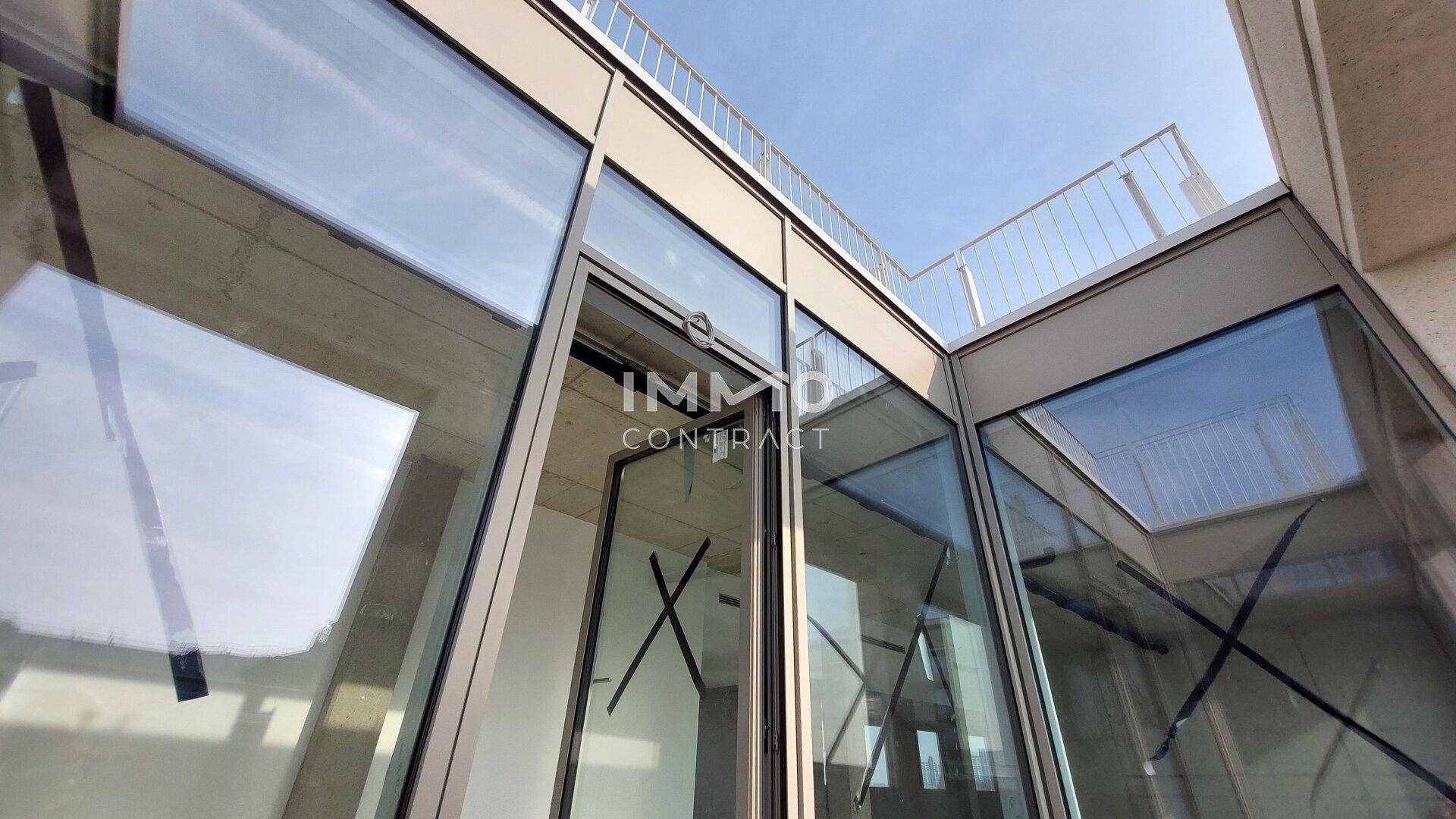 Moderne Glasfassade eines Bürogebäudes mit klarem Himmel und einem Balkongeländer im oberen Bereich.