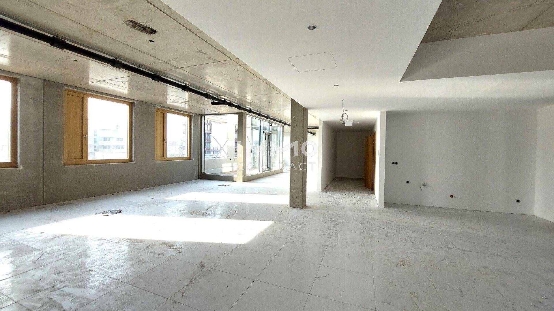 Großer, offener Büroraum mit Fliesenboden, Betonwänden und einer modernen Glasfront.