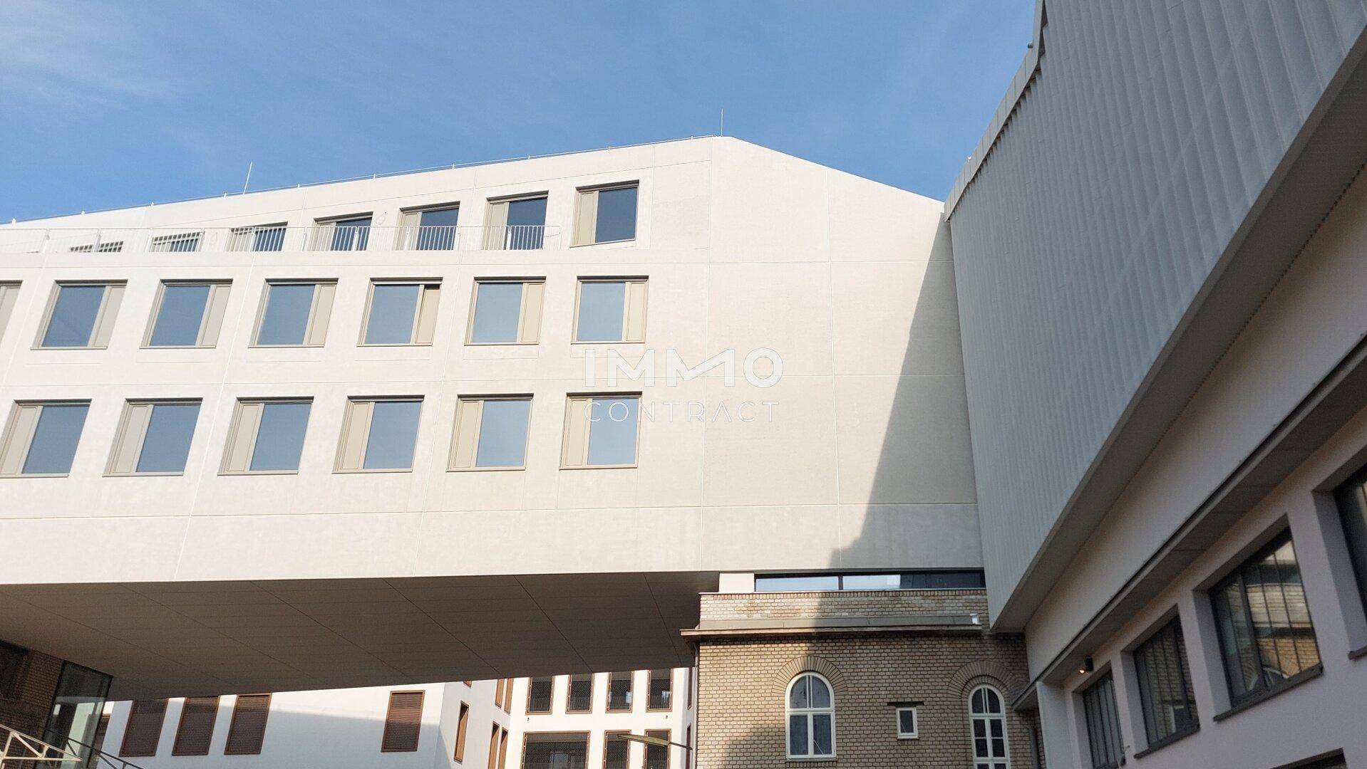 Moderne Architektur mit markanter, auskragender Fassade und vielen Fenstern über einem Altbau.