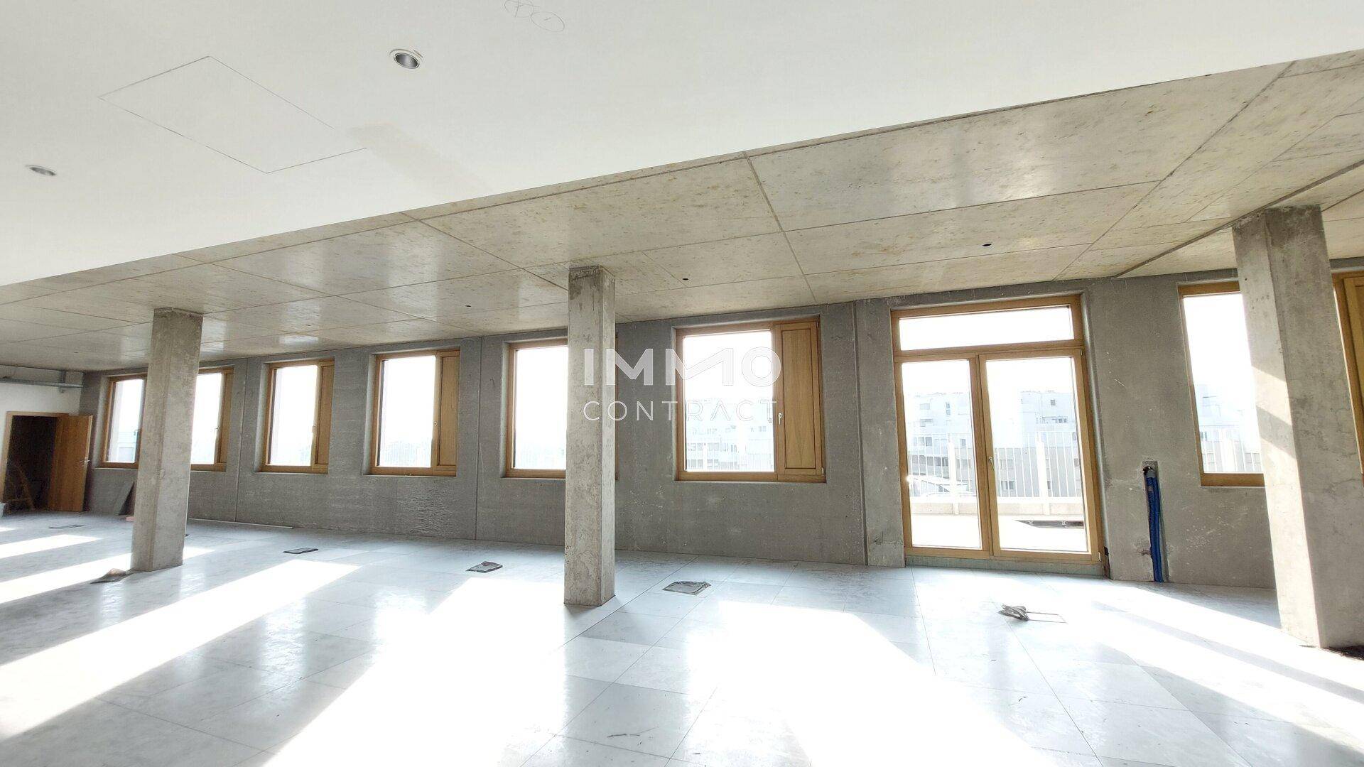 Großer, heller Büroraum im Rohbau mit Betonwänden, Säulen und vielen Fenstern, bereit für den Ausbau.