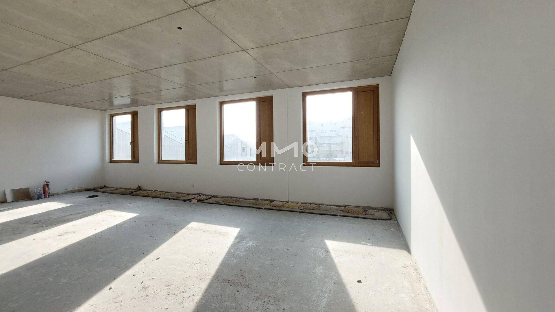 Heller, unmöblierter Büroraum mit Betonboden, weißen Wänden und einer Reihe von Fenstern, ideal für individuelle Gestaltung.