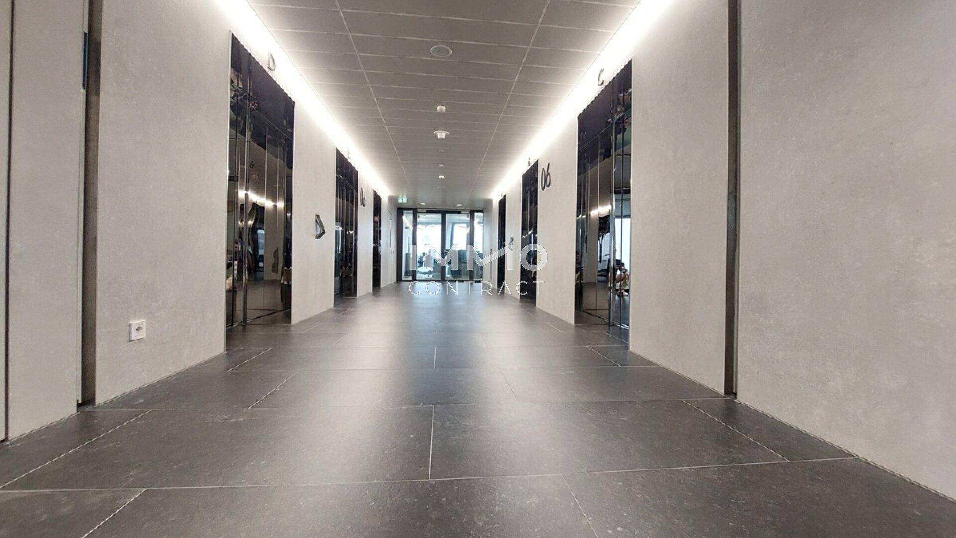 Langer, moderner Büroflur mit dunklen Fliesen, hellen Wänden und integrierter Deckenbeleuchtung.