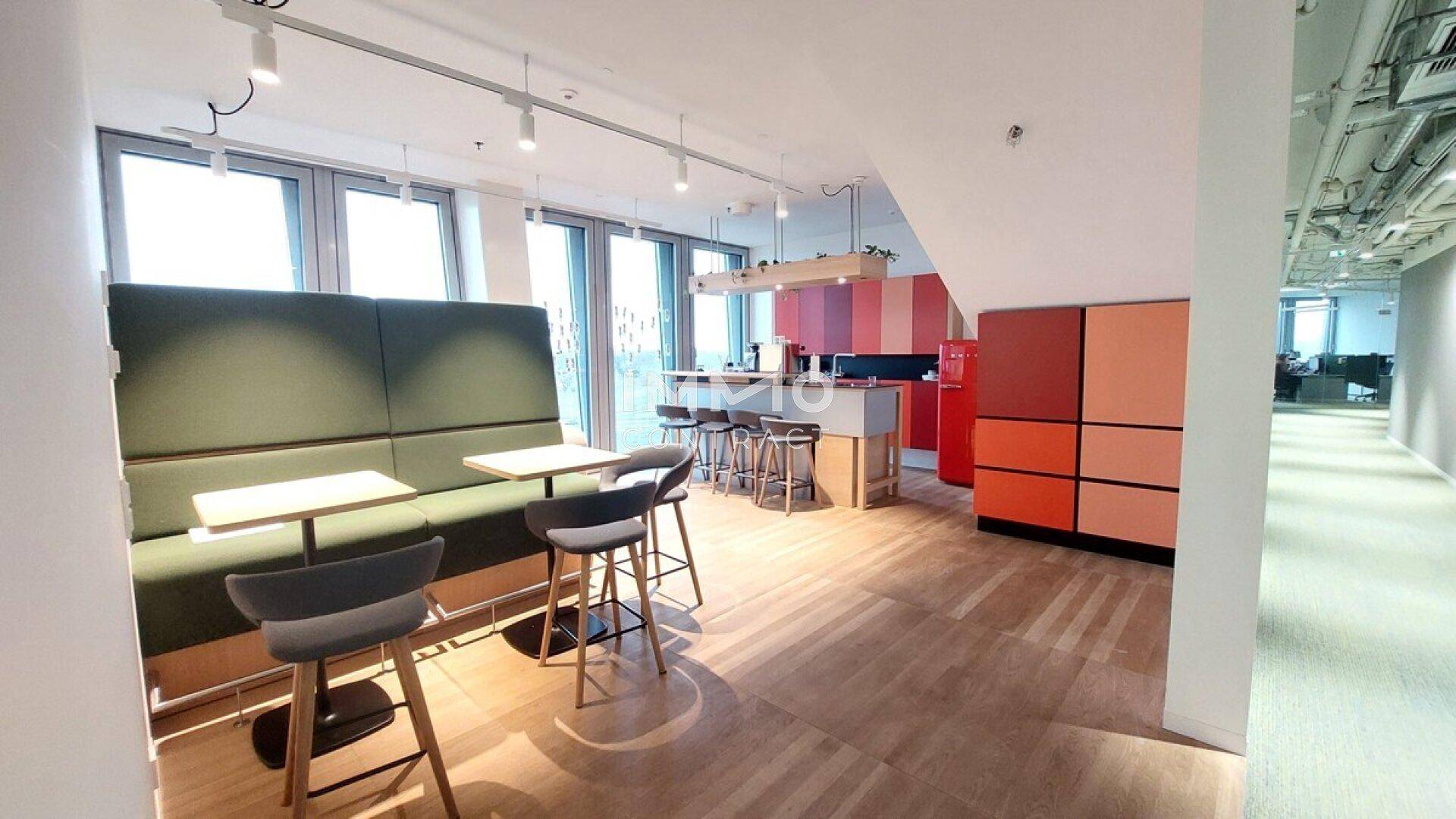 Farbenfroher Pausenbereich mit Sitzbänken, Bartischen und einer modernen Küchenzeile mit Holzboden.