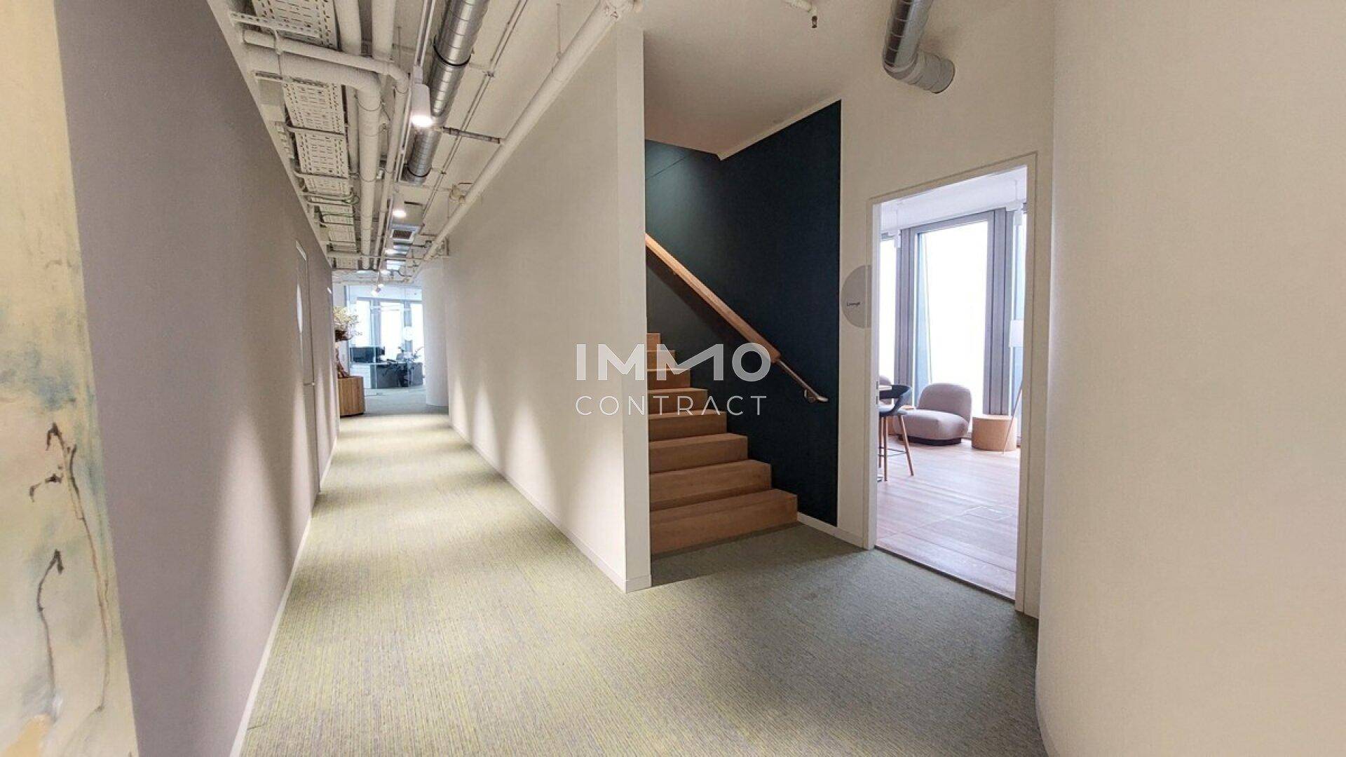 Bürogang mit einer Holztreppe und Zugang zu einem weiteren Raum mit Sitzgelegenheiten.