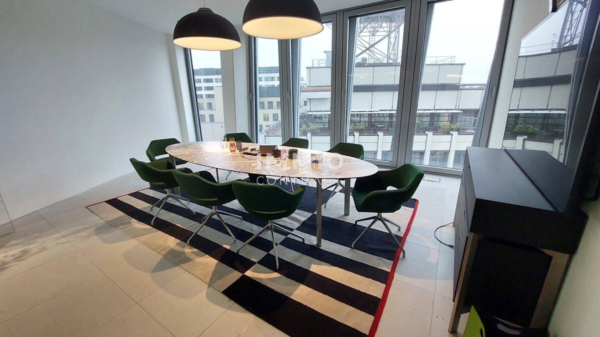 Eleganter Konferenzraum mit ovalem Tisch, grünen Stühlen und Blick auf die umliegenden Gebäude.