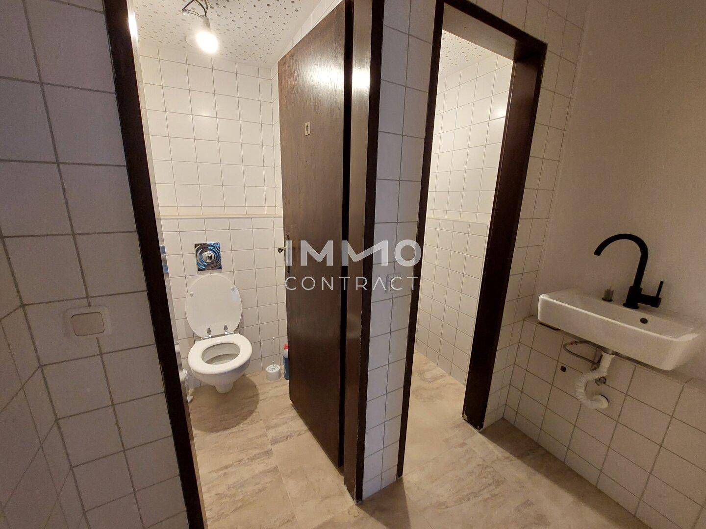 Einfache Toilettenanlage mit Waschbecken und gefliesten Wänden in hellem Design, funktional und sauber.