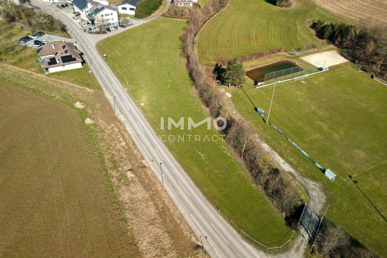 Luftbild des weitläufigen Grüngeländes mit Straße, Sportanlagen und angrenzenden Wohnhäusern in der Ferne.