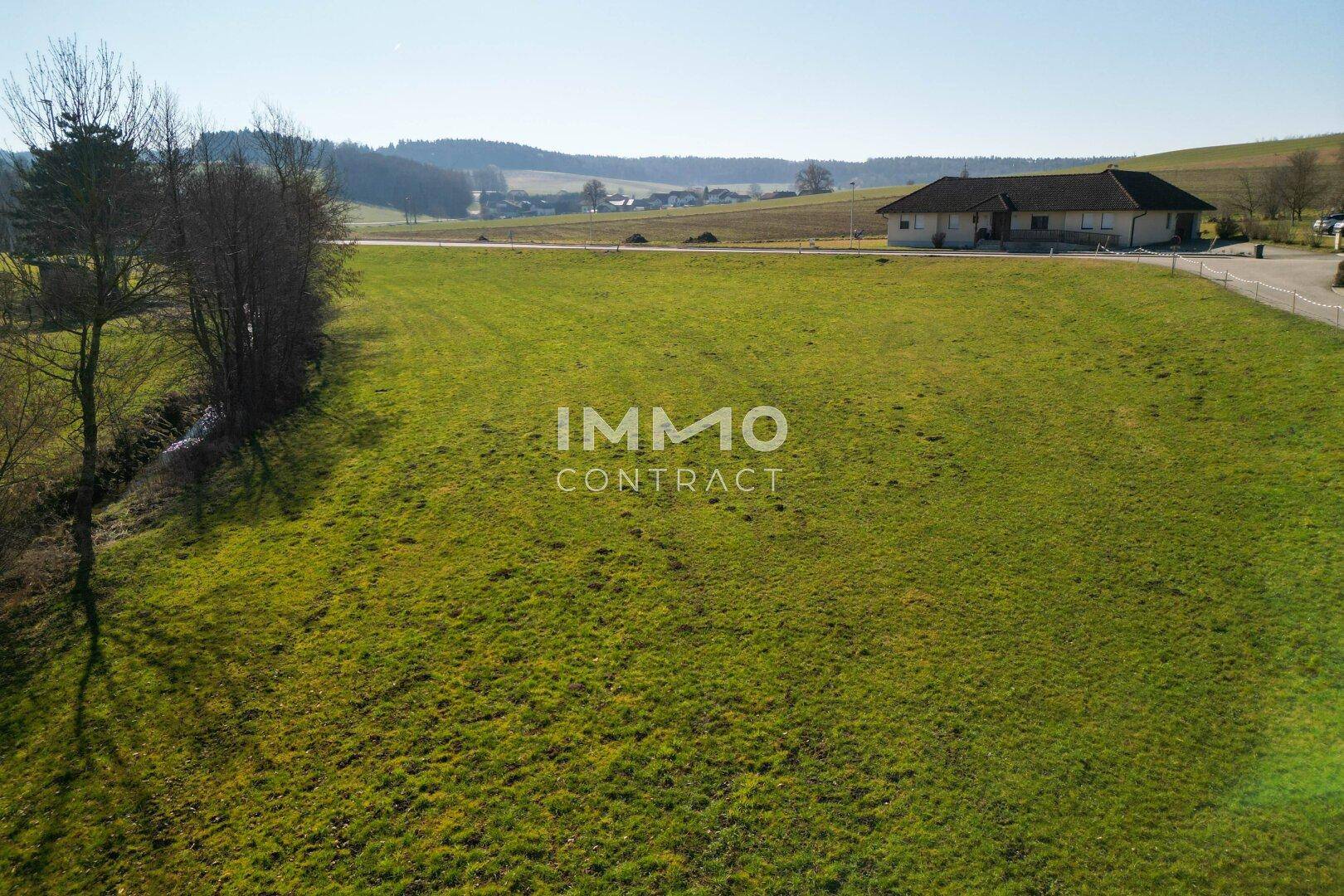 Großes, sonniges Grüngelände mit weitem Blick auf die hügelige Landschaft und ein entferntes Gebäude.
