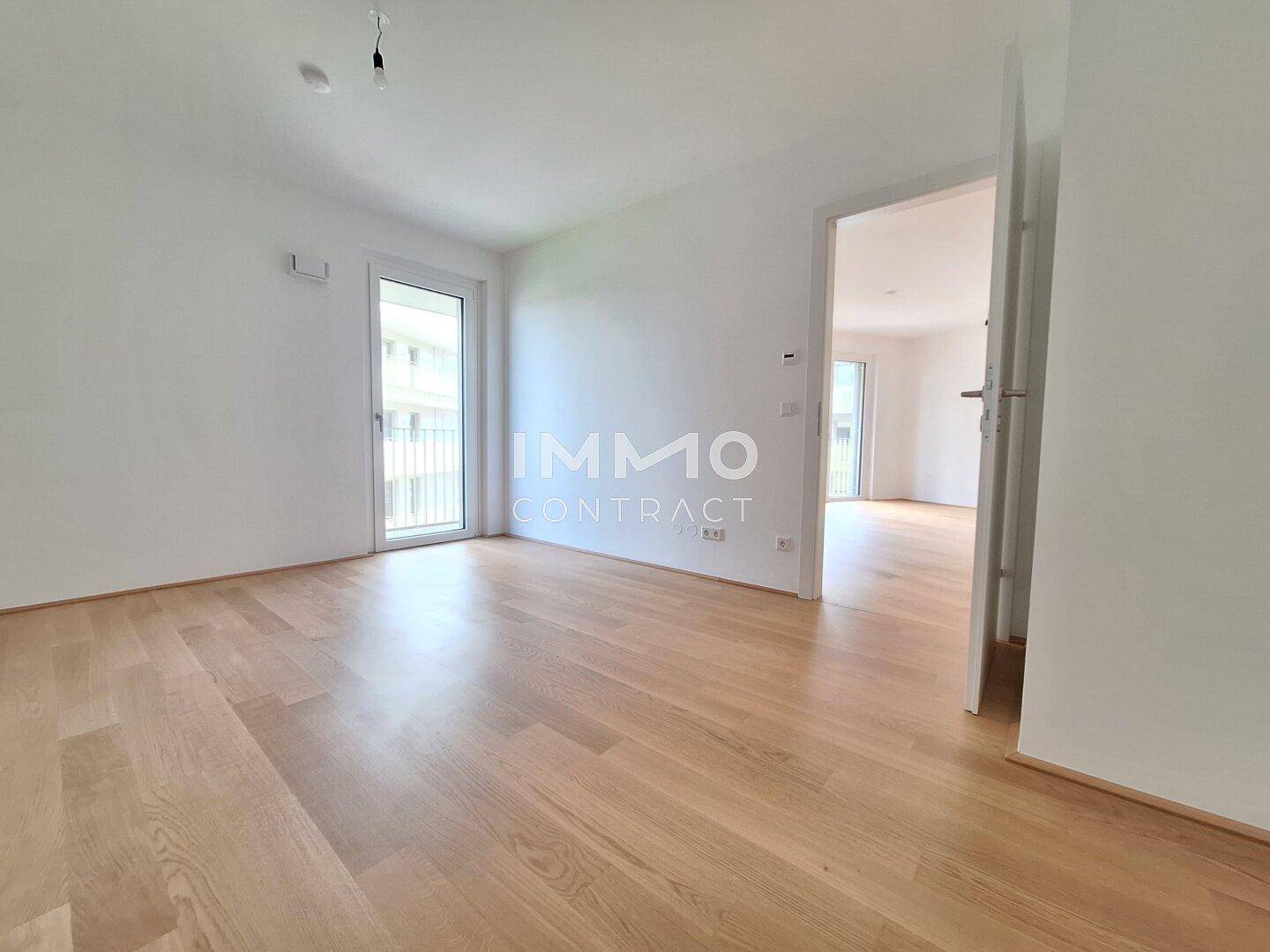 Leerer Raum mit Holzboden und Balkonzugang, der viel natürliches Licht hereinlässt.