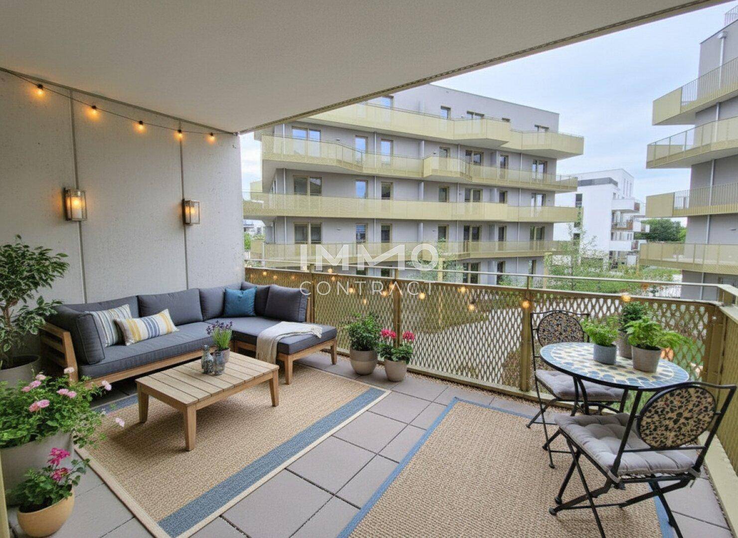 Möblierter Balkon mit gemütlicher Sitzecke, Pflanzen und Blick auf moderne Gebäude.