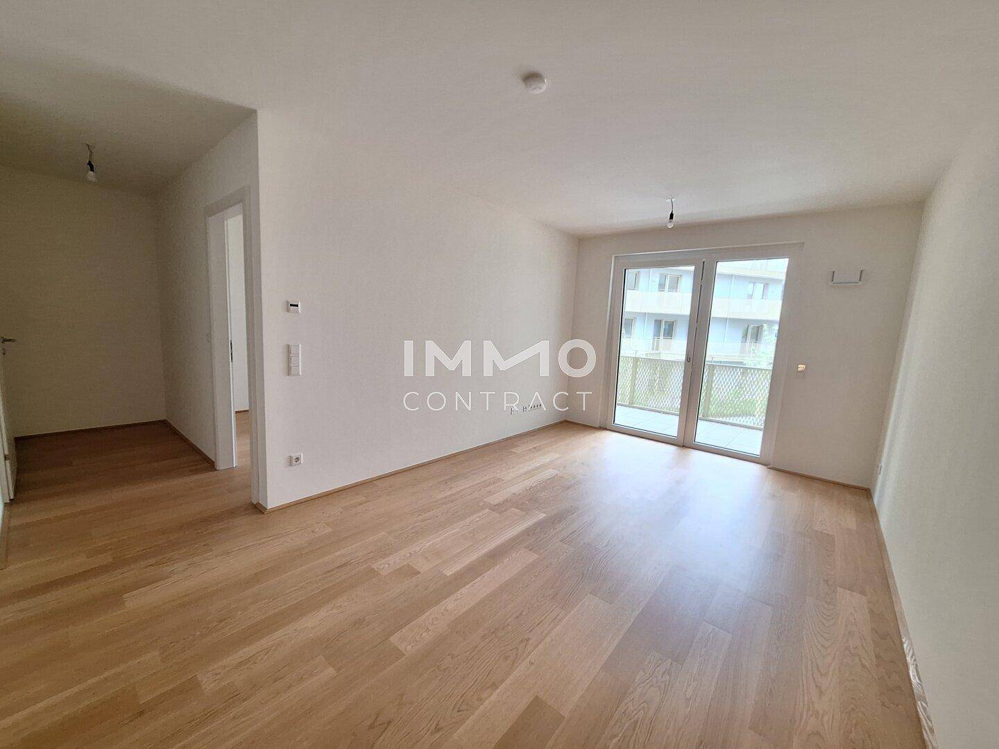 Geräumiges, unmöbliertes Wohnzimmer mit Holzboden und Zugang zu einem Balkon.
