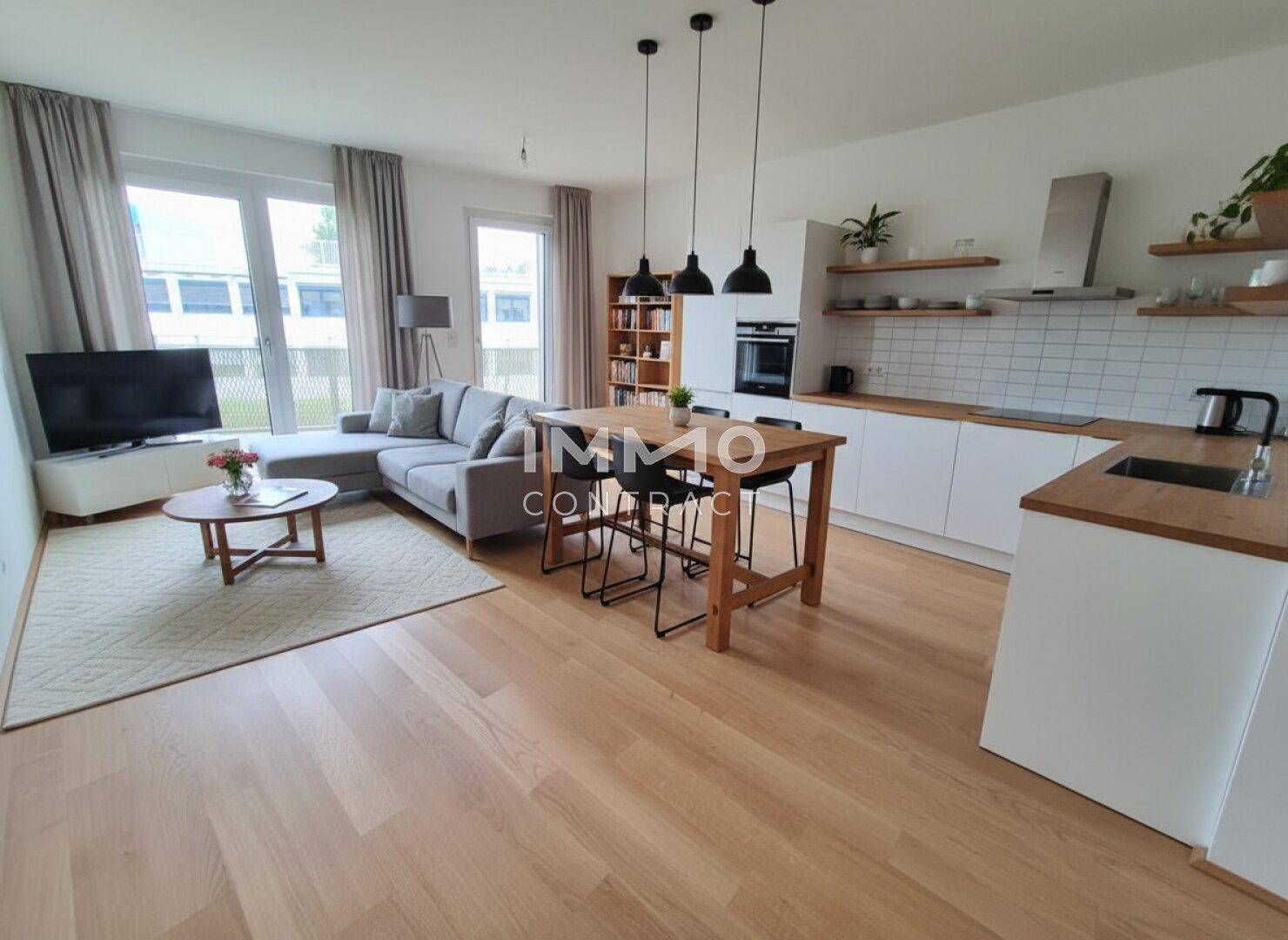 Moderner offener Wohn-Essbereich mit integrierter weißer Küche, Holzboden und viel Tageslicht.