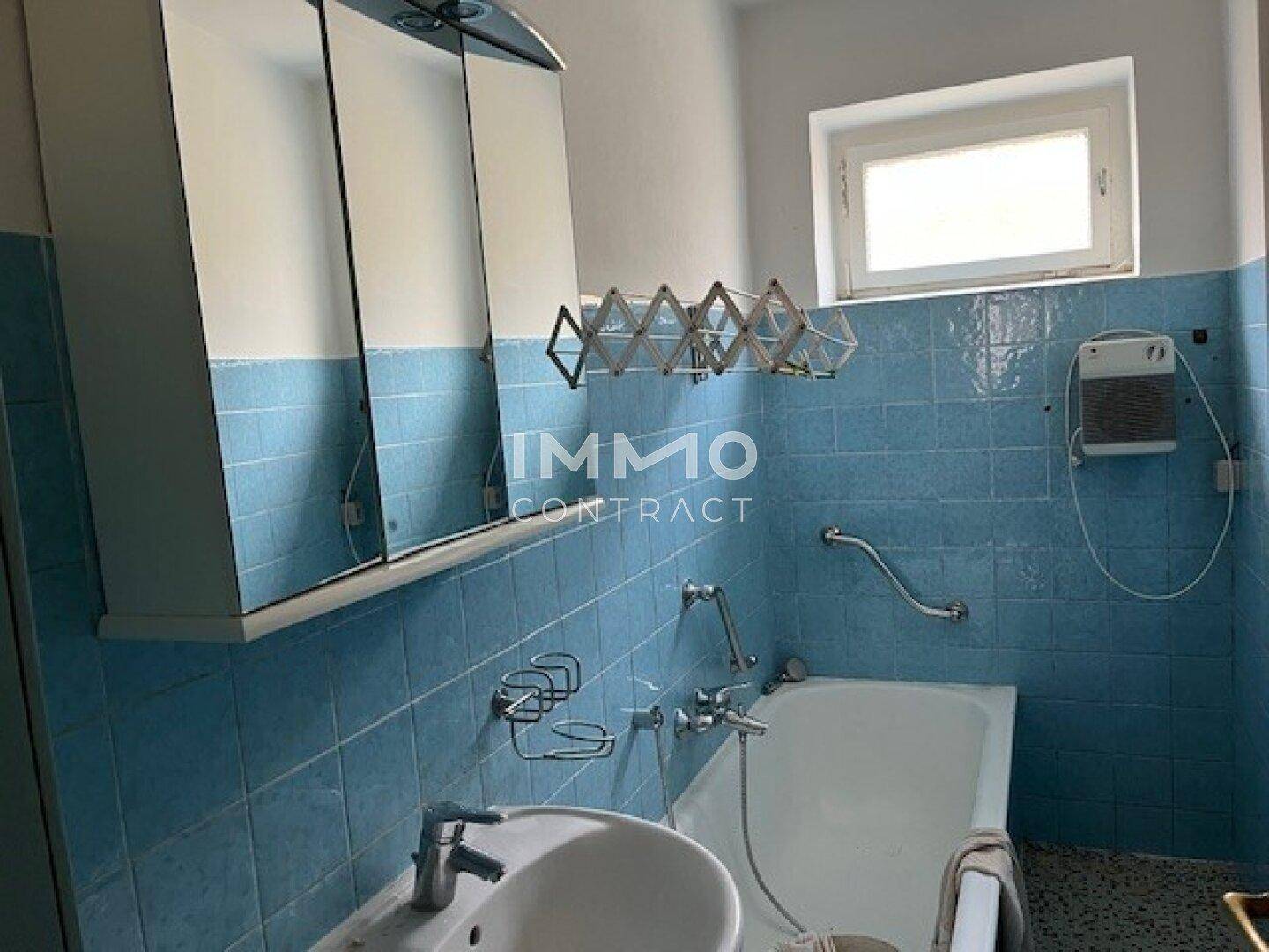 Badezimmer mit blauen Fliesen, Badewanne, Waschbecken und Fenster.