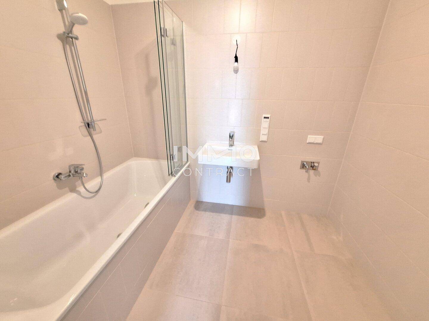 Modernes Badezimmer mit Badewanne, integrierter Dusche und hellem Fliesenboden, ausgestattet mit einem Einzelwaschbecken.