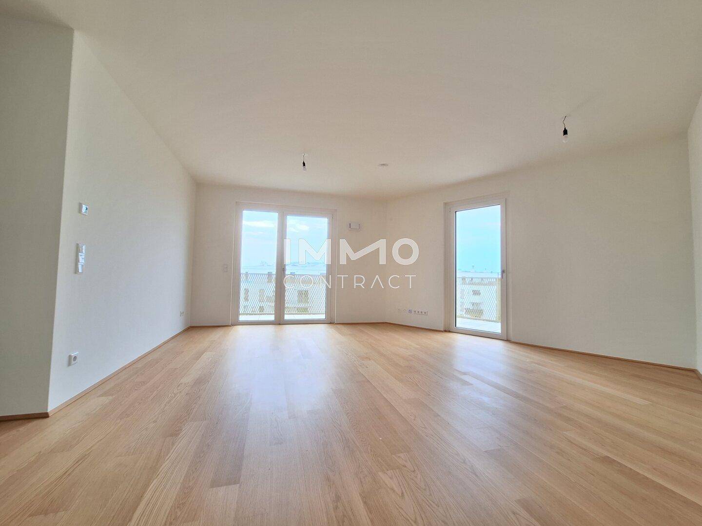 Geräumiges, leeres Wohnzimmer mit hellem Parkettboden und großen Fenstern.
