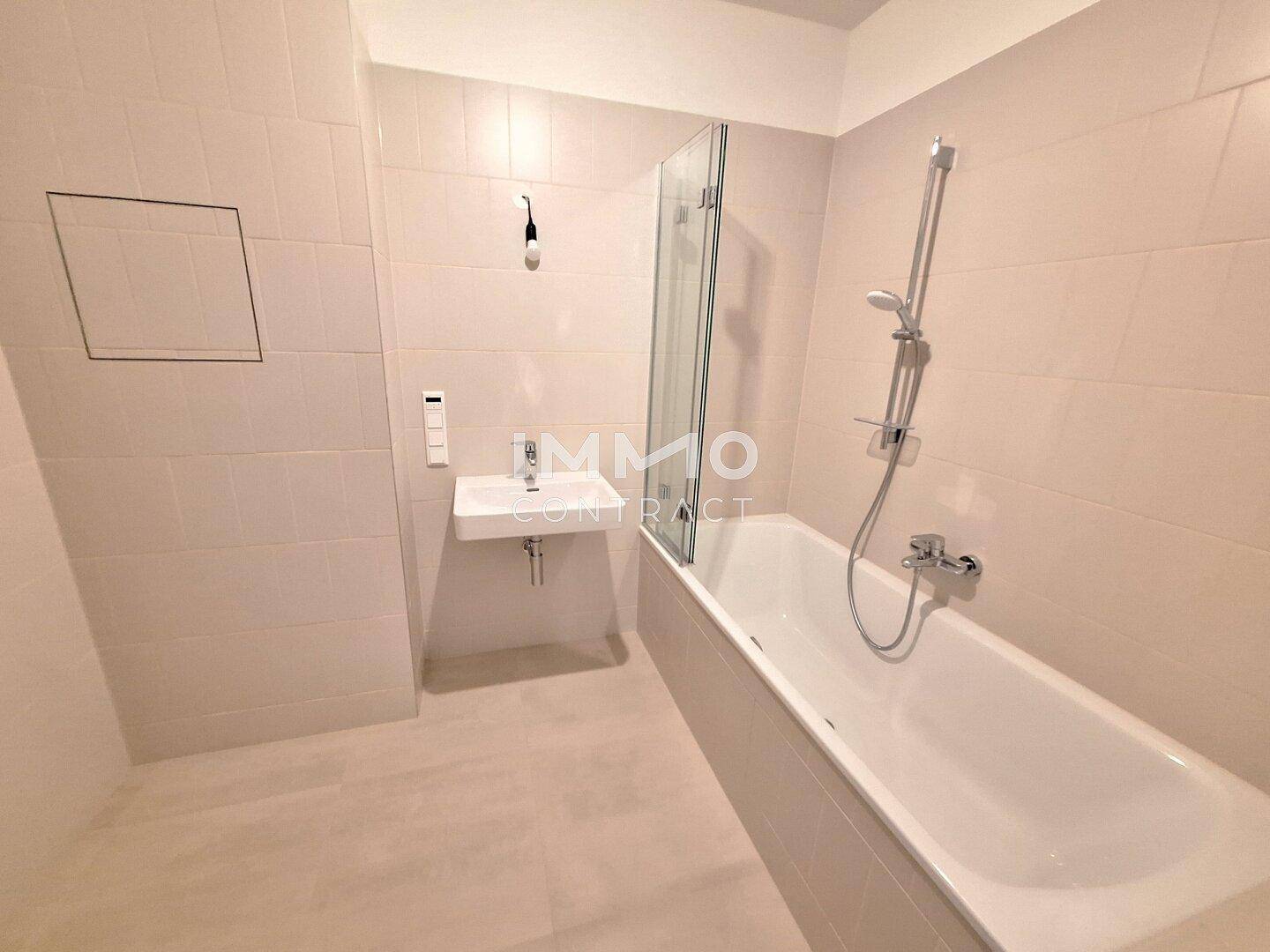 Modernes Badezimmer mit Badewanne, Dusche und Wandwaschbecken in hellen Fliesen.